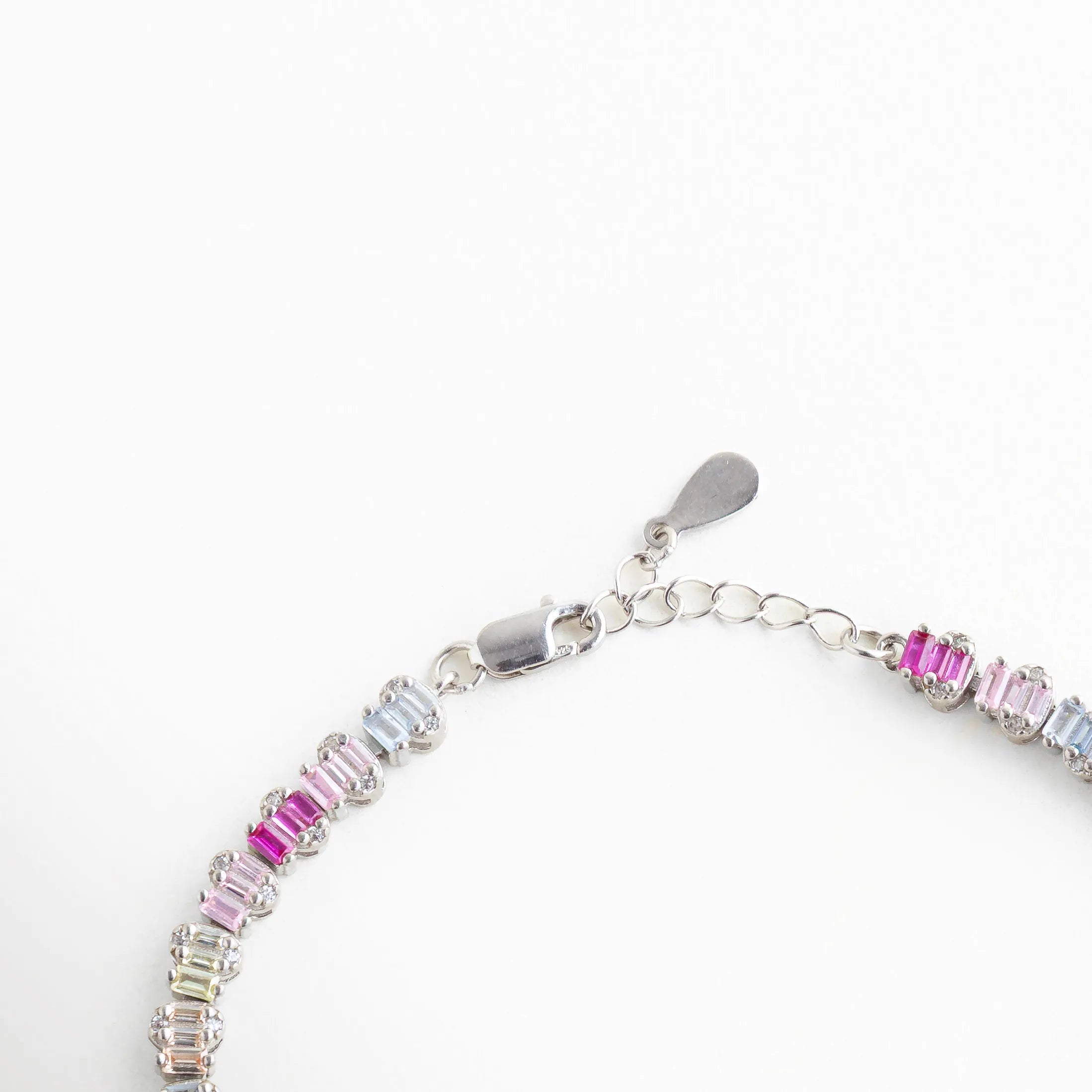 Detalle del broche tipo langosta y cadena de extensión en pulsera de plata 925, Cierre ajustable de joyería con acabado en oro blanco y placa de autenticidad, Vista técnica del sistema de ajuste para diferentes medidas de muñeca en brazalete de plata, Broche seguro y eslabones finales de pulsera de circonias multicolor, Reverso del cierre de la pulsera resaltando el pulido del baño de oro blanco.