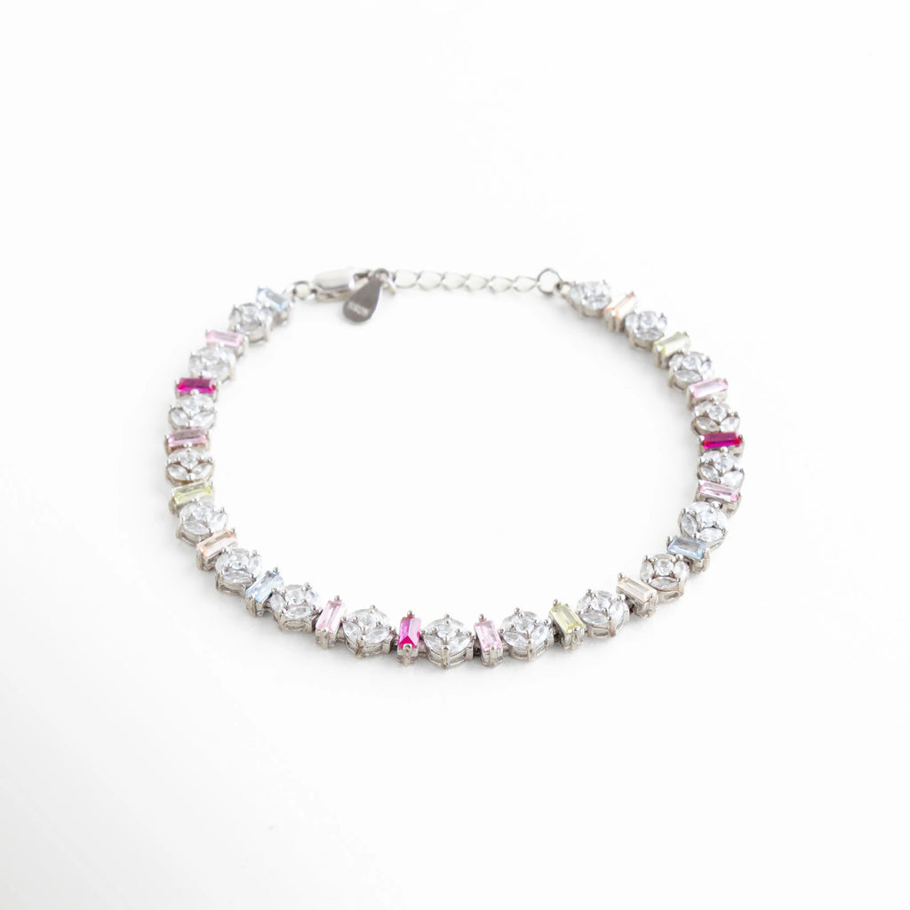 Perspectiva angular de pulsera resaltando el relieve y brillo de las circonias baguette, Pulsera de lujo accesible en oro blanco con piedras rosas y moradas, Vista en 45 grados de brazalete brillante de plata con diseño de arcoíris pastel, Joyería de moda: pulsera delgada de plata con piedras rectangulares de colores, Ángulo lateral que muestra la precisión del engaste en la pulsera de oro blanco.