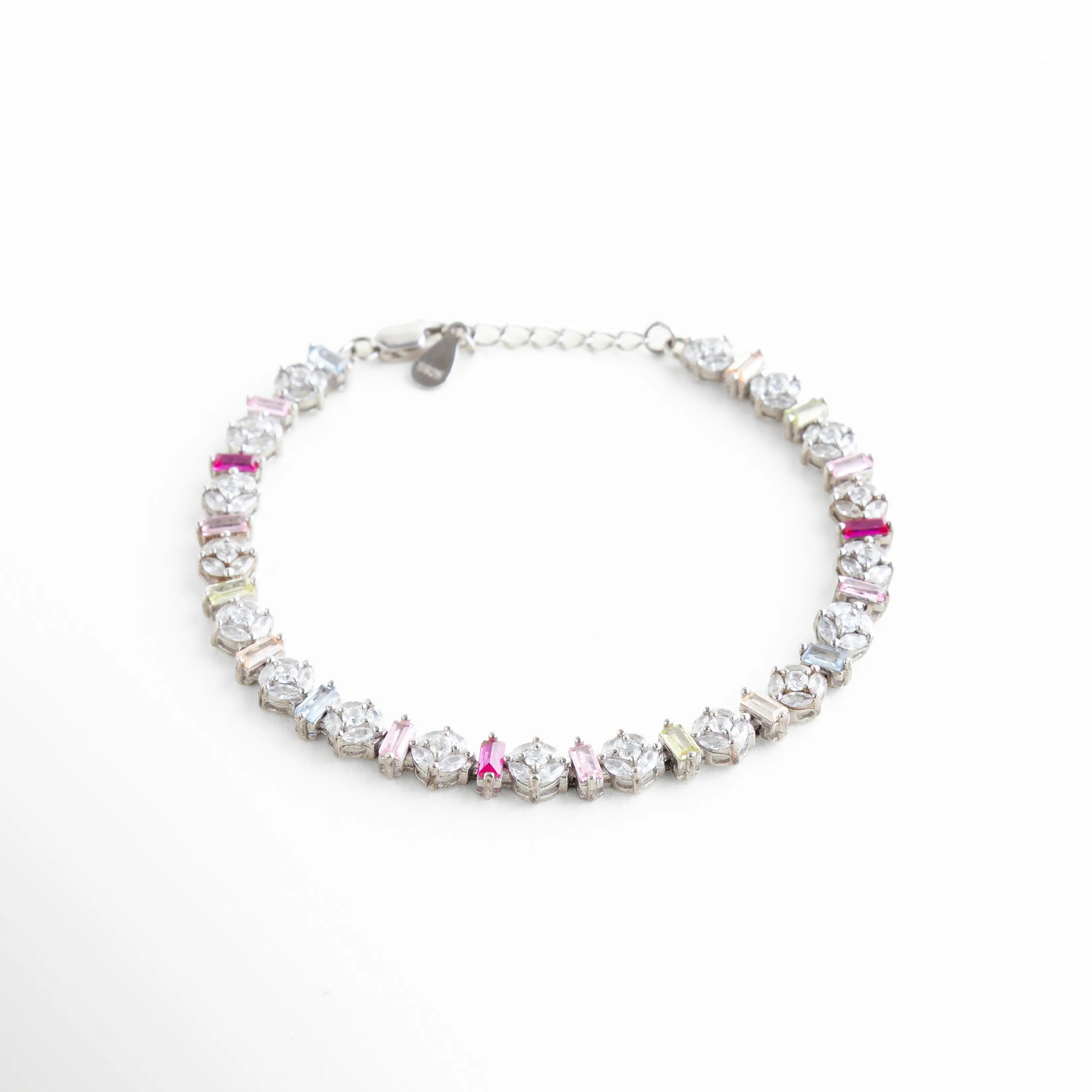 Perspectiva angular de pulsera resaltando el relieve y brillo de las circonias baguette, Pulsera de lujo accesible en oro blanco con piedras rosas y moradas, Vista en 45 grados de brazalete brillante de plata con diseño de arcoíris pastel, Joyería de moda: pulsera delgada de plata con piedras rectangulares de colores, Ángulo lateral que muestra la precisión del engaste en la pulsera de oro blanco.