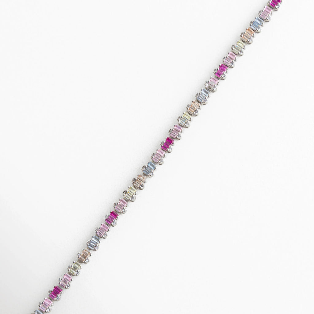 Pulsera de Plata 925 con baño de oro blanco y hileras de circonias en corte baguette horizontal, Detalle de brazalete plateado con degradado de circonias en tonos fucsia, lila y lavanda, Primer plano de pulsera con piedras rectangulares de colores vibrantes y acabado en oro blanco, Joyería de plata ley 925: brazalete moderno con circonias multicolor de alta calidad, Vista macro de las incrustaciones de circonia baguette en pulsera de plata ajustable.