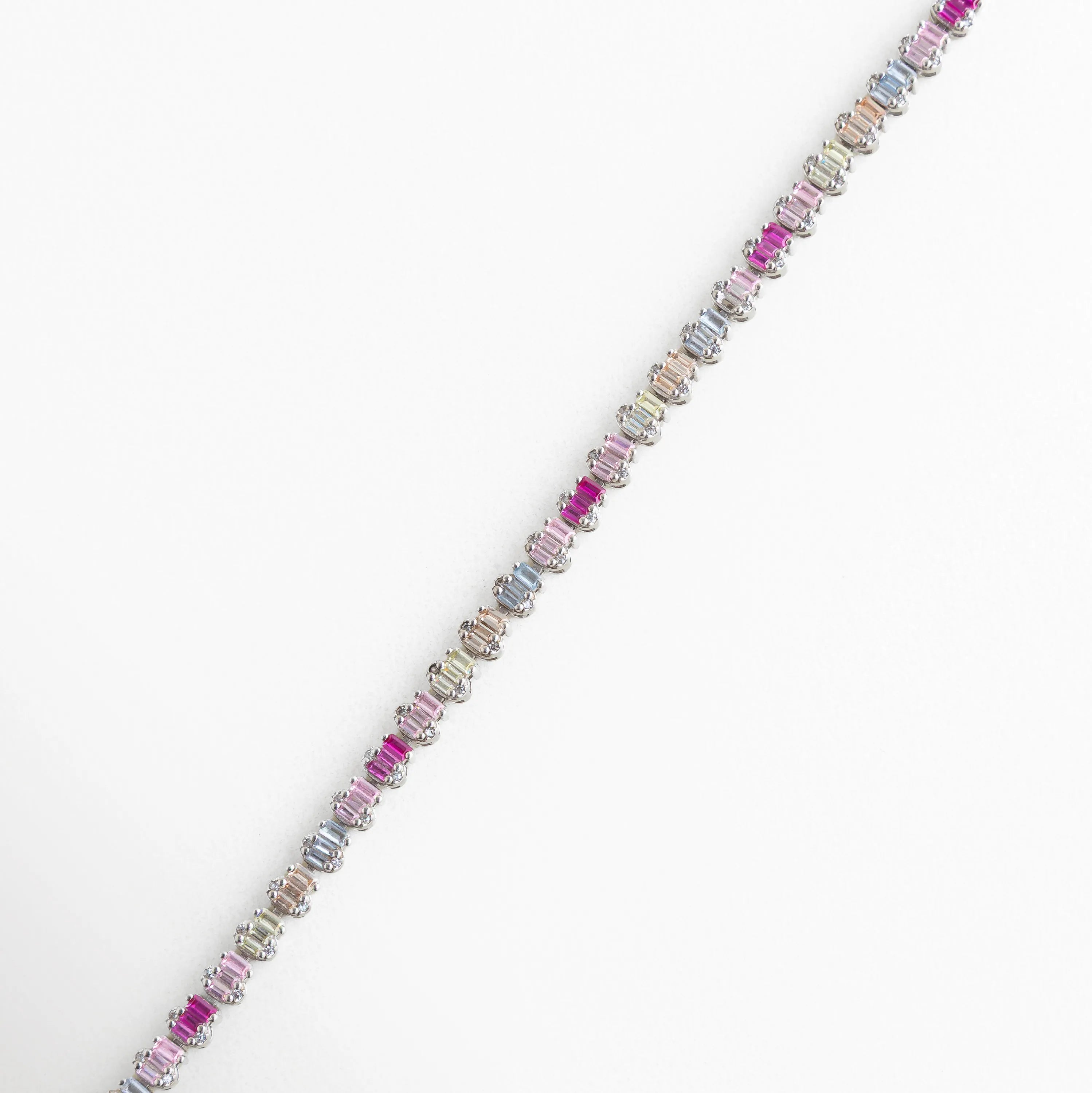 Pulsera de Plata 925 con baño de oro blanco y hileras de circonias en corte baguette horizontal, Detalle de brazalete plateado con degradado de circonias en tonos fucsia, lila y lavanda, Primer plano de pulsera con piedras rectangulares de colores vibrantes y acabado en oro blanco, Joyería de plata ley 925: brazalete moderno con circonias multicolor de alta calidad, Vista macro de las incrustaciones de circonia baguette en pulsera de plata ajustable.
