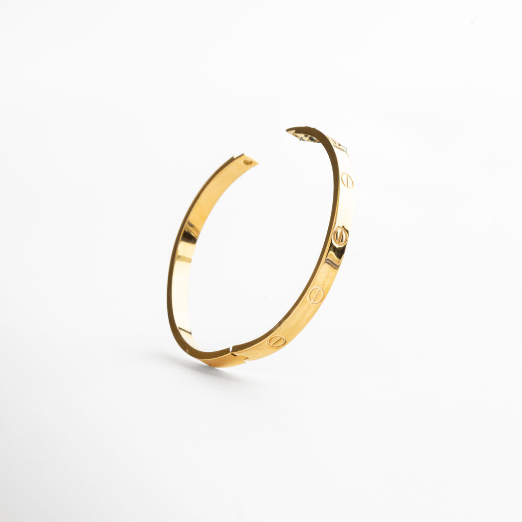 cierre rígido del brazalete dorado, sistema de apertura metálico en oro 18K, detalle del broche estructurado dorado, cierre minimalista en brazalete contemporáneo, mecanismo de ajuste del brazalete rígido dorado