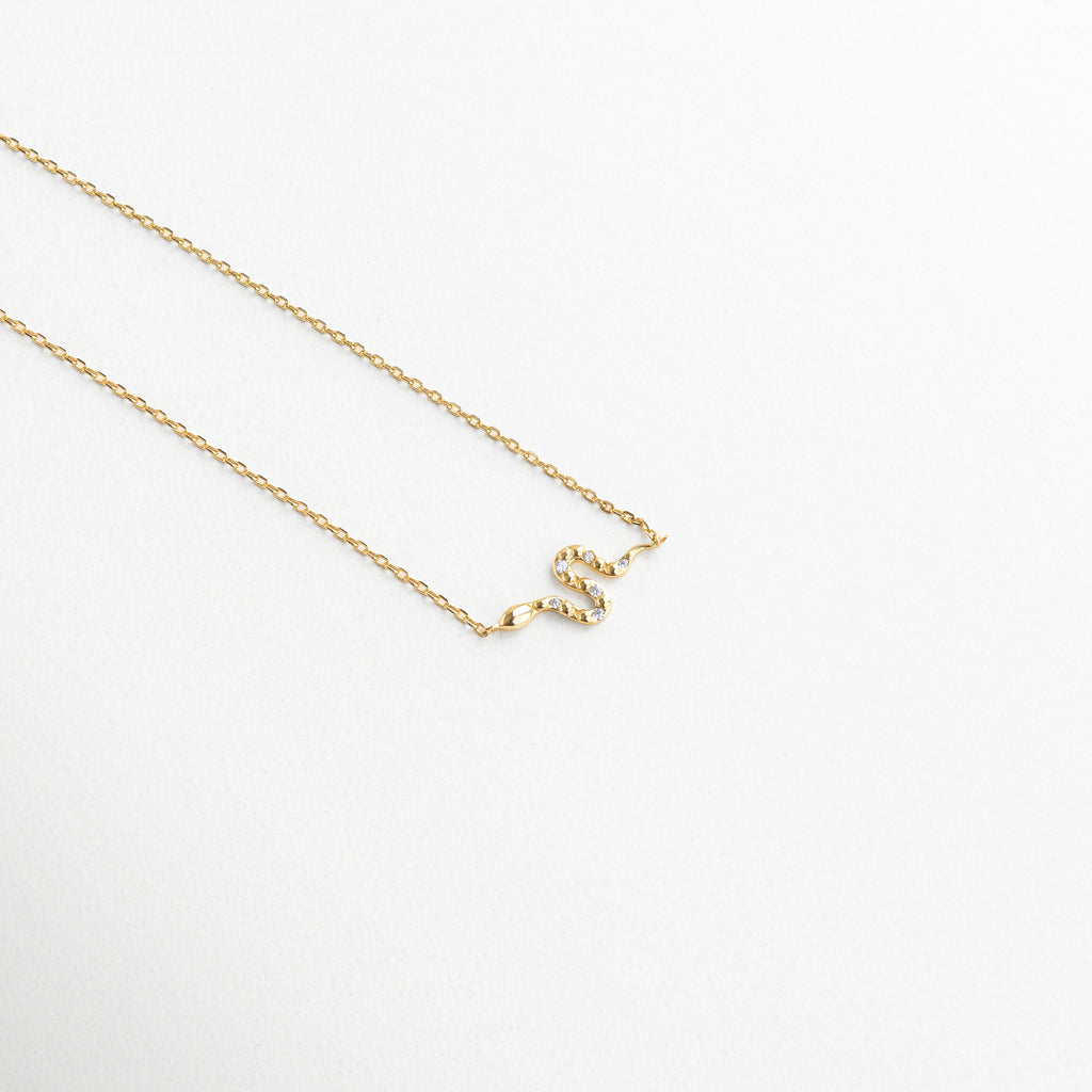 Dije de serpiente dorado con incrustaciones de zirconias, Detalle del colgante con forma de serpiente brillante, Primer plano de serpiente miniatura en collar dorado, Diseño delicado de serpiente con textura brillante