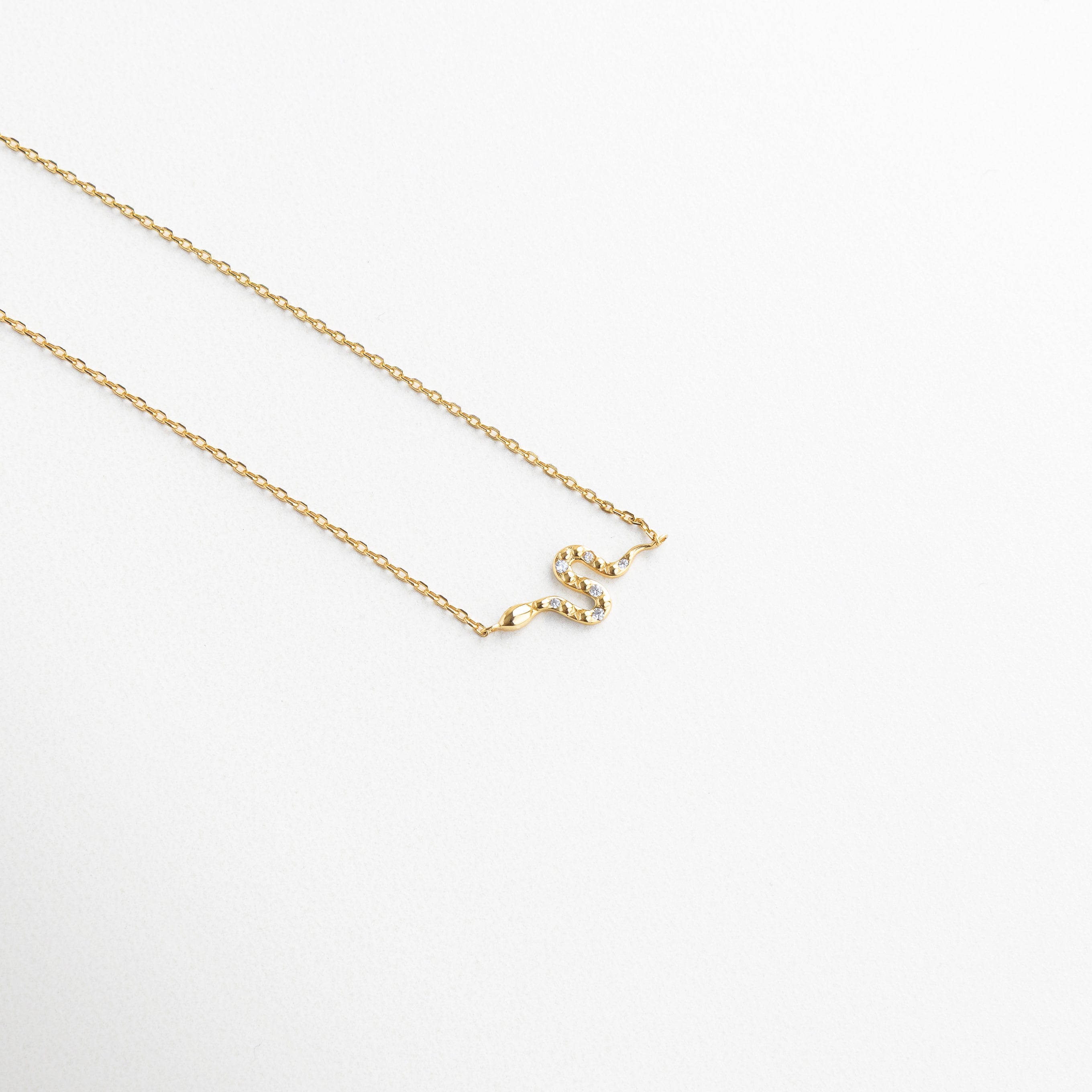 Dije de serpiente dorado con incrustaciones de zirconias, Detalle del colgante con forma de serpiente brillante, Primer plano de serpiente miniatura en collar dorado, Diseño delicado de serpiente con textura brillante