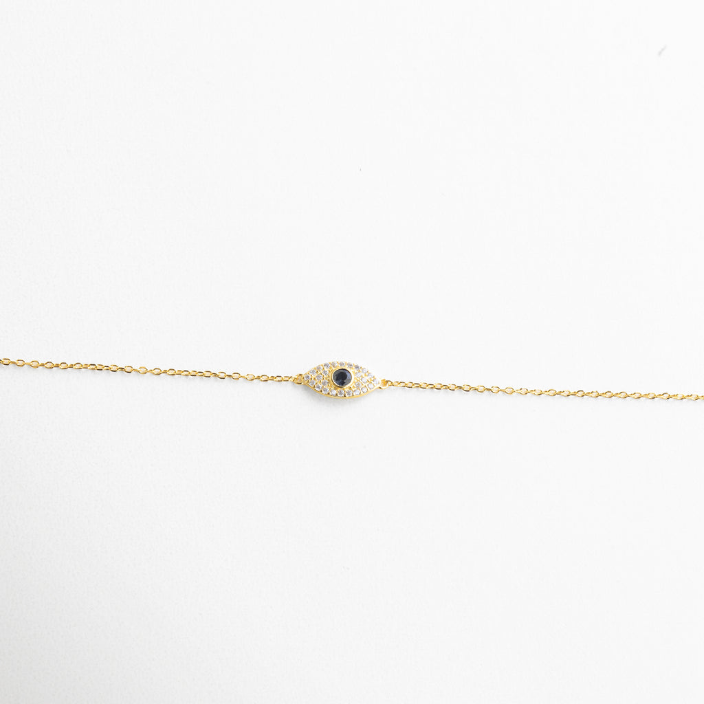 Textura metálica suave y forma curva del amuleto, Incrustaciones bien alineadas con brillo discreto, Contorno del ojo con diseño limpio y elegante, Unión sutil entre cadena y dije protector, Acabado sereno que refleja la luz con sutileza