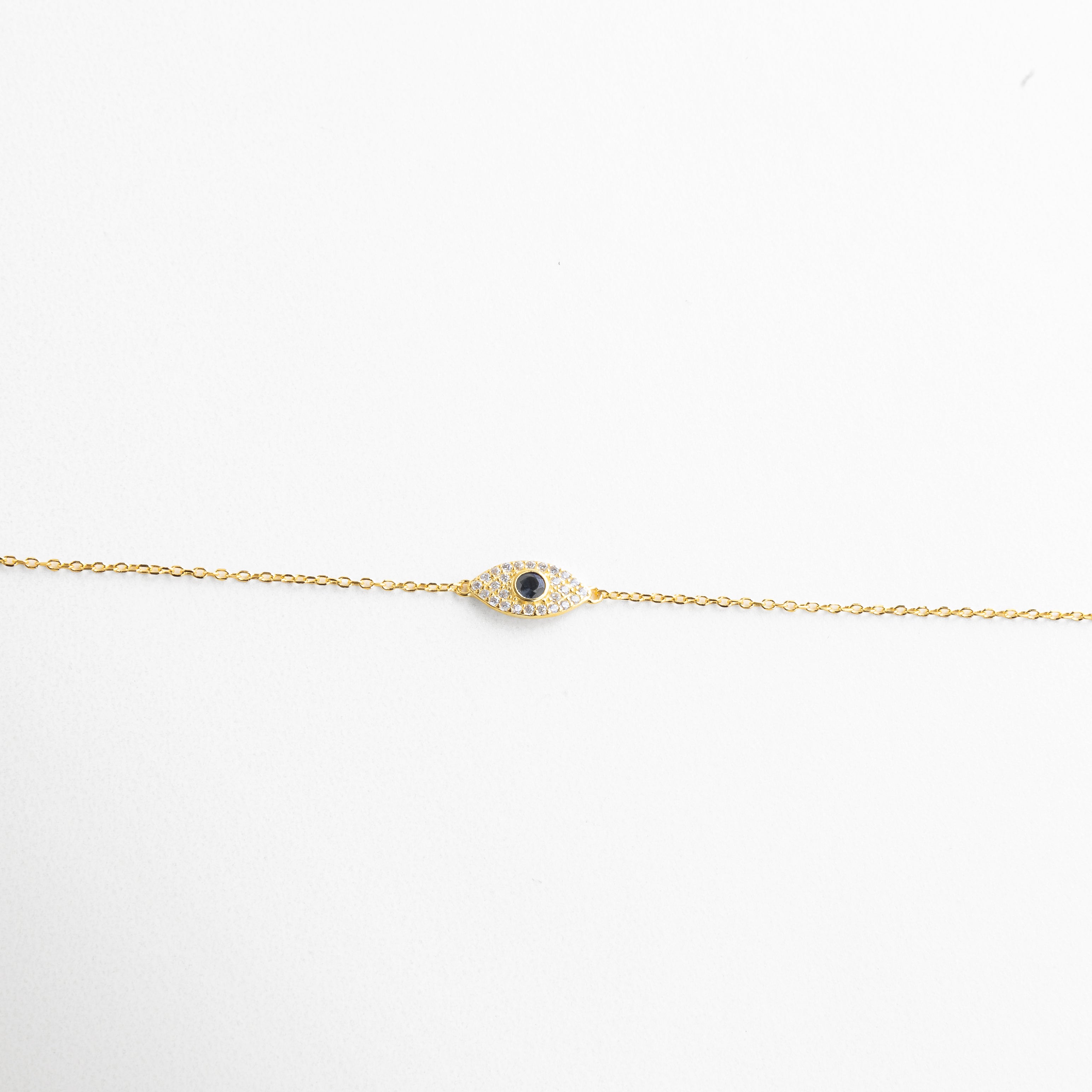 Textura metálica suave y forma curva del amuleto, Incrustaciones bien alineadas con brillo discreto, Contorno del ojo con diseño limpio y elegante, Unión sutil entre cadena y dije protector, Acabado sereno que refleja la luz con sutileza