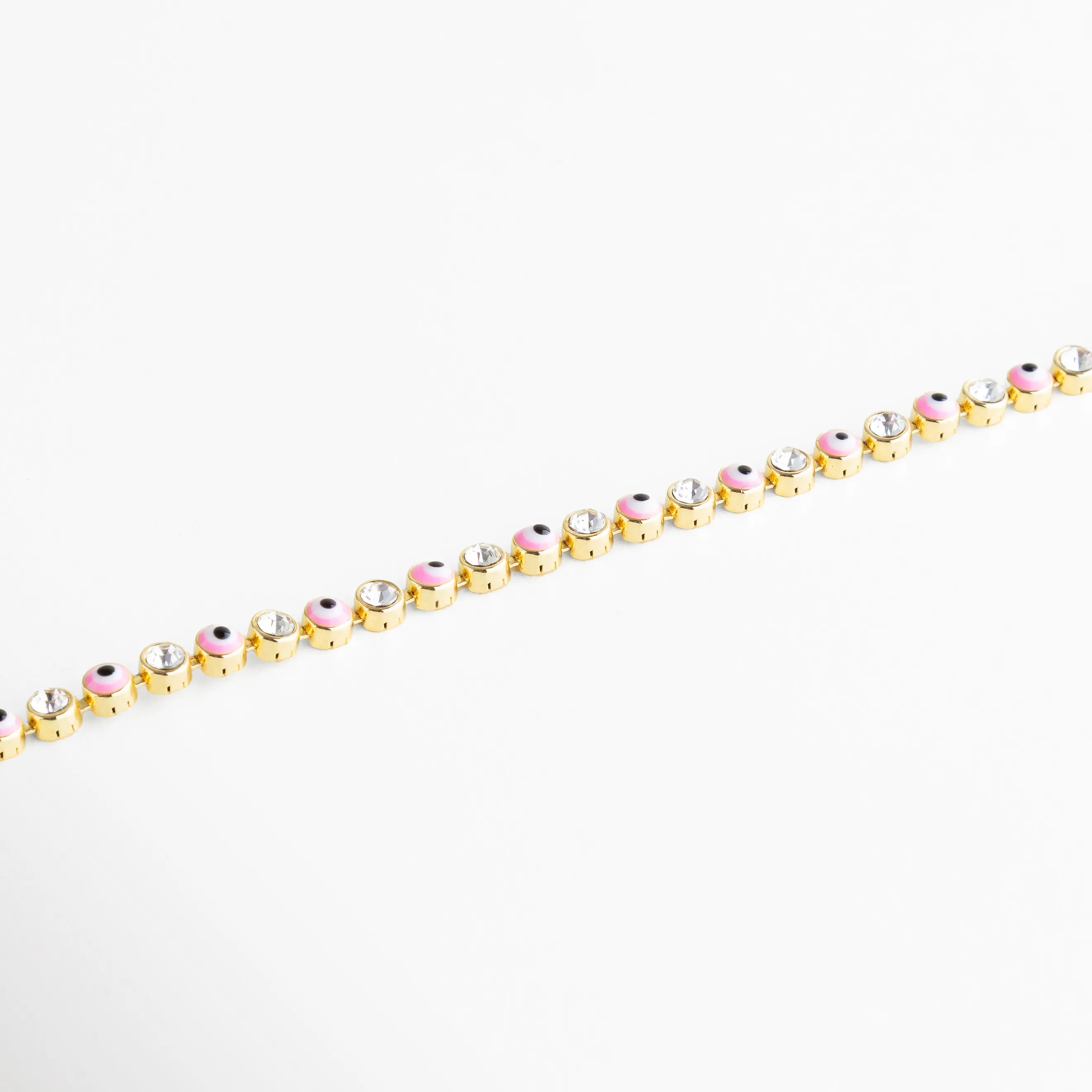 Pulsera dorada decorada con charms de ojito rosa y cristales transparentes, una pieza divertida y protectora.