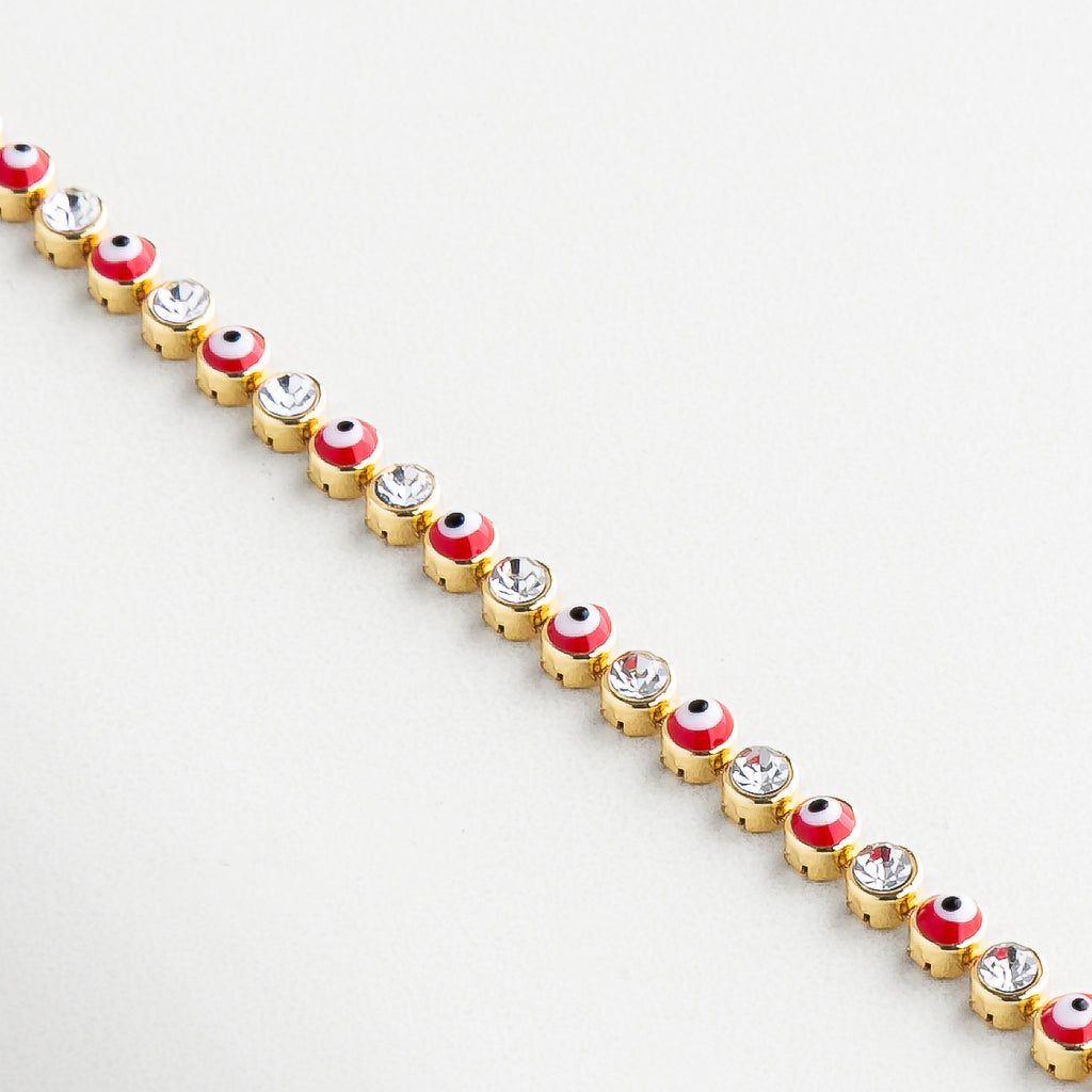 Ojo turco dorado con centro de zirconia brillante, Incrustaciones delicadas en los dijes de protección, Charms de ojos con contorno definido y textura lisa, Contraste entre el rojo intenso y el dorado pulido, Zirconias alineadas con brillo sutil