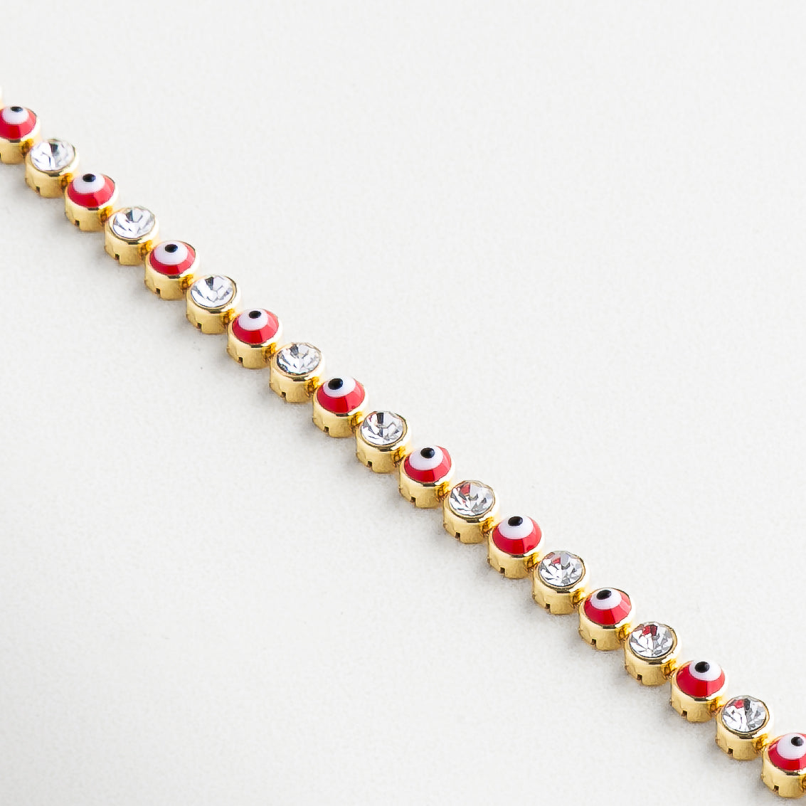 Ojo turco dorado con centro de zirconia brillante, Incrustaciones delicadas en los dijes de protección, Charms de ojos con contorno definido y textura lisa, Contraste entre el rojo intenso y el dorado pulido, Zirconias alineadas con brillo sutil
