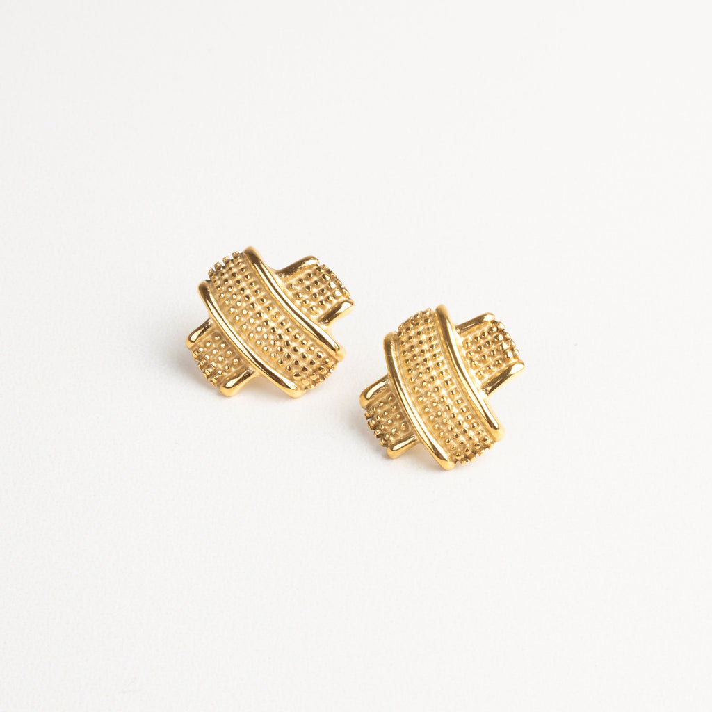 Vista frontal de aretes tipo tacha dorados con textura, diseño moderno y elegante.