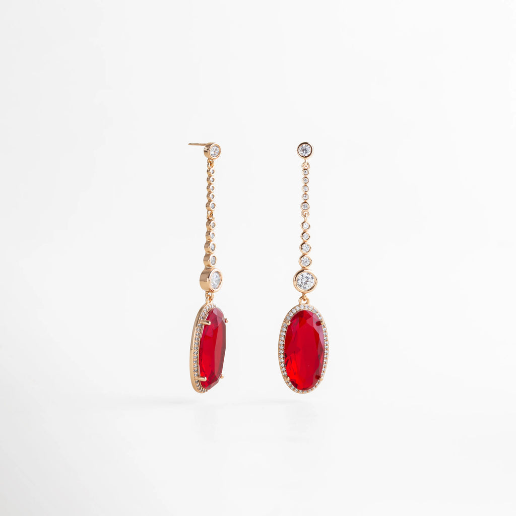 aretes largos dorados con piedra roja ovalada colgante, cadena de zirconias, vista lateral mostrando grosor y caída, fondo blanco, joyería elegante