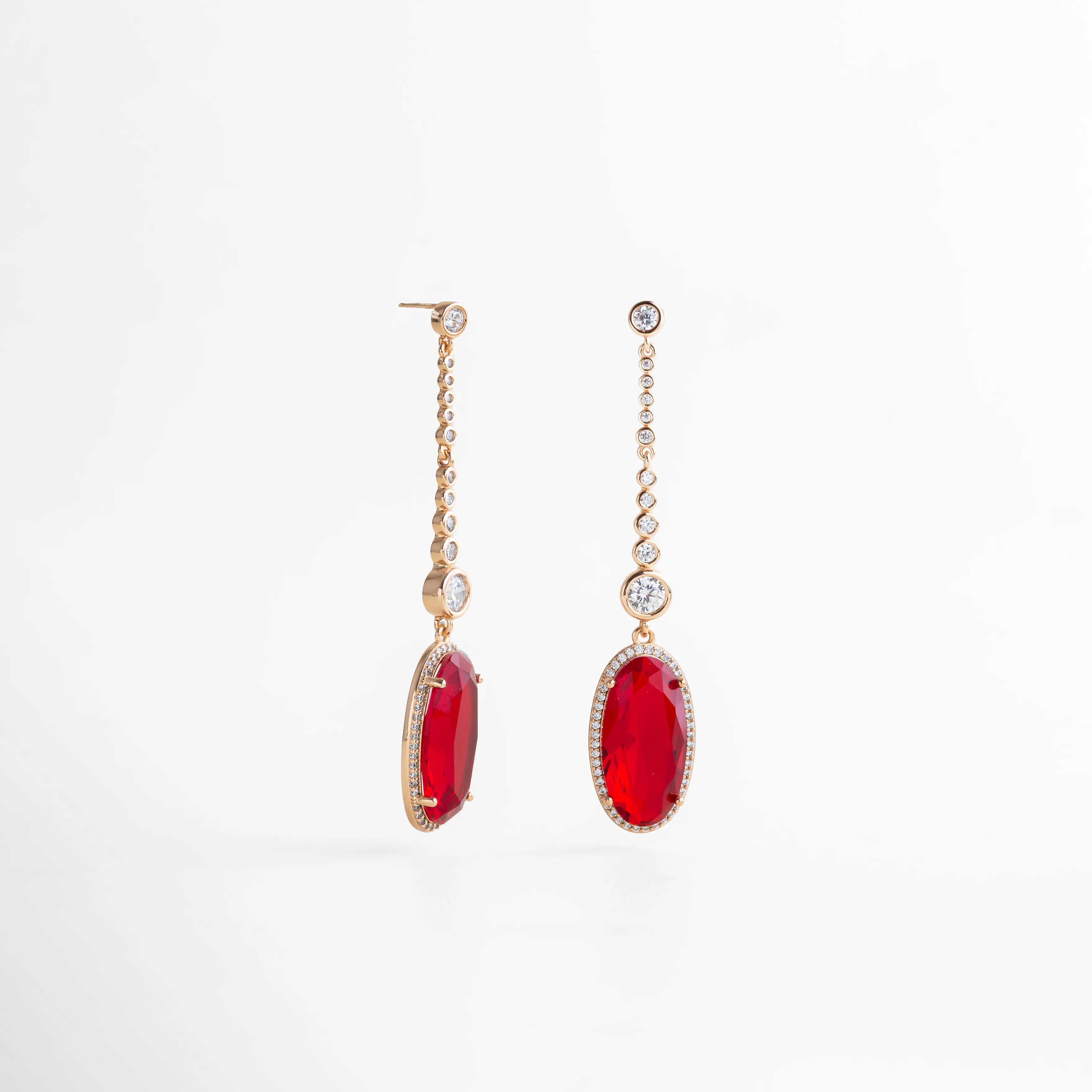 aretes largos dorados con piedra roja ovalada colgante, cadena de zirconias, vista lateral mostrando grosor y caída, fondo blanco, joyería elegante