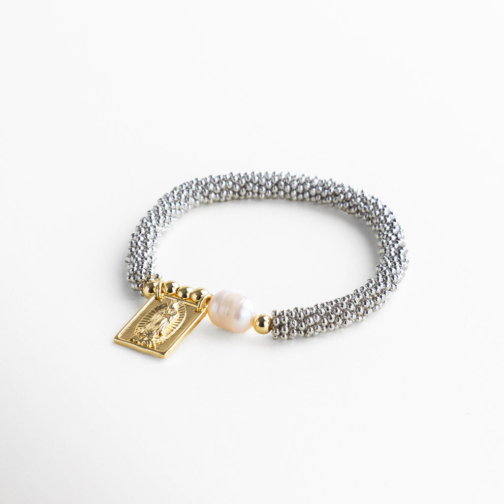 Perfil delgado que permite un uso cómodo y discreto, Pulsera flexible que se ajusta fácilmente a diferentes tamaños de muñeca, Acabado brillante que refleja la luz con sutileza desde todos los ángulos, Estructura resistente que mantiene su forma con el uso diario, Diseño equilibrado entre símbolo religioso y estética moderna