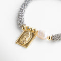 Pulsera elástica con diseño simbólico de protección espiritual, Baño en chapa de oro 18K que aporta un acabado brillante y duradero, Detalle central con imagen de la Virgen María, símbolo de fe y esperanza, Incrustación de perla sintética que añade un toque delicado y elegante, Ideal para quienes buscan un accesorio con significado y estilo