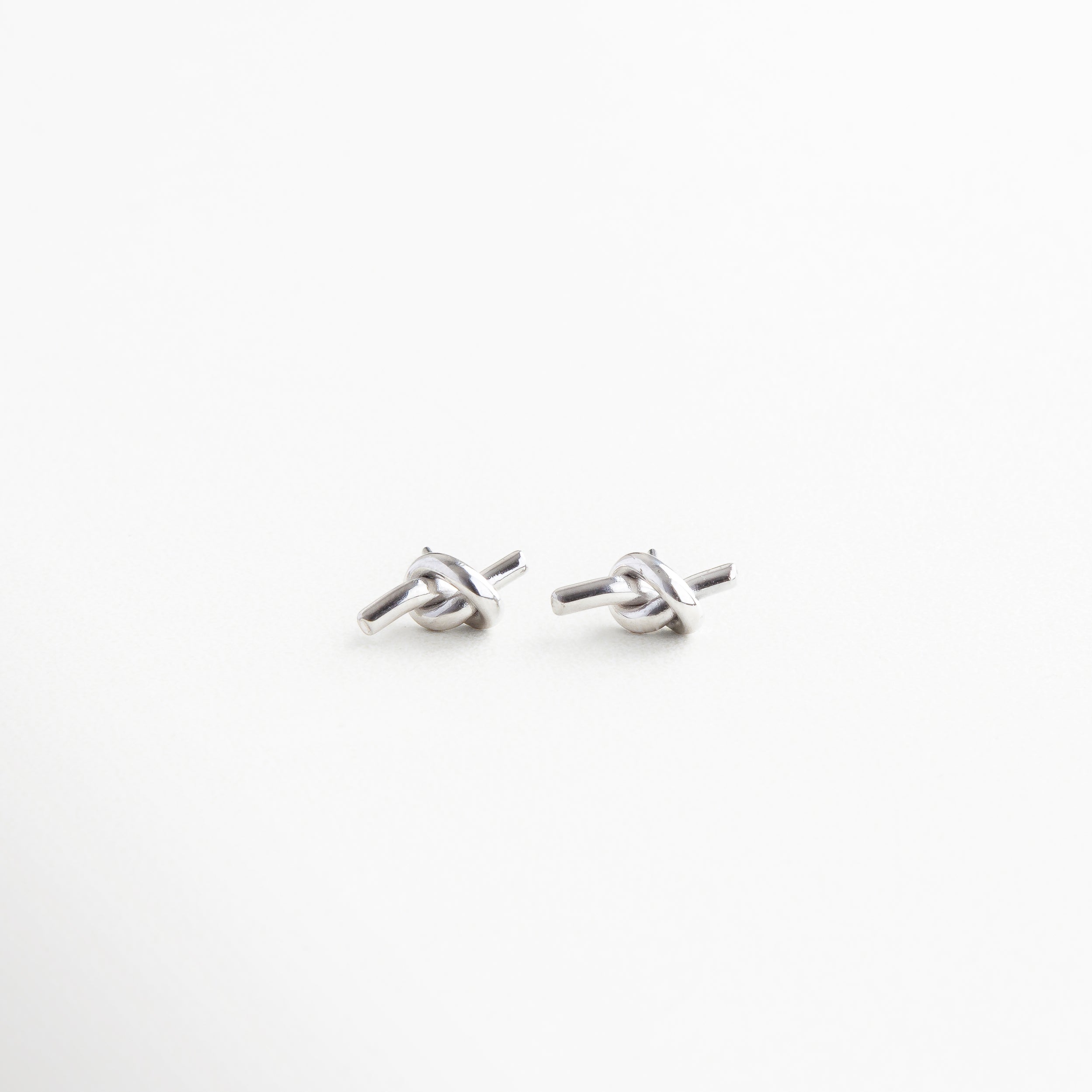 Aretes con diseño de nudo entrelazado y acabado brillante, Par de aretes elegantes estilo nudo con forma clásica, Aretes entrelazados con diseño simbólico y sofisticado, Joyería de diseño fluido con forma de lazo estilizado