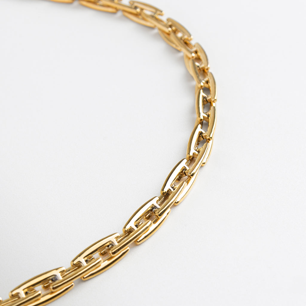 Collar Amelia Golden con volumen desde ángulo lateral, Diseño estructurado en dorado visto en perspectiva,Eslabones dorados con forma moderna en vista inclinada, Collar de acero con chapa de oro en ángulo decorativo