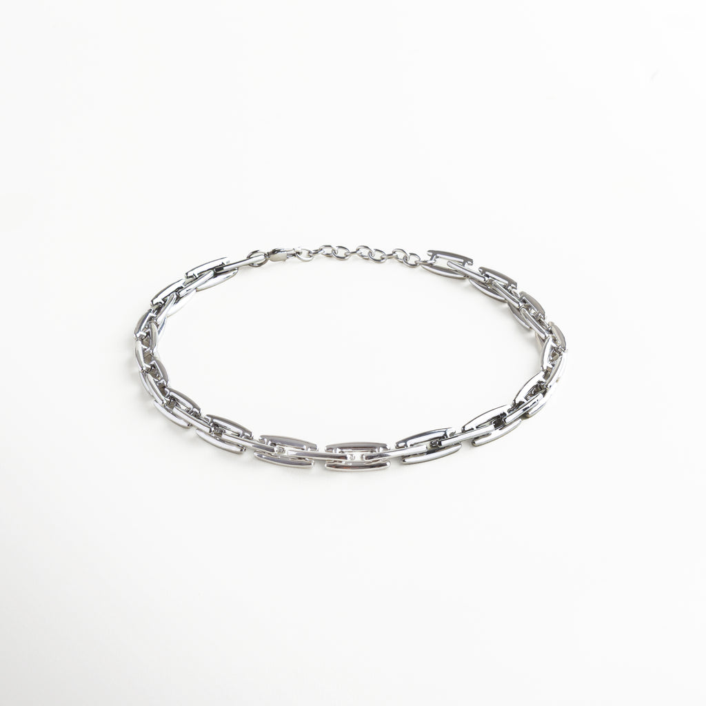 Collar plateado, cadena plateada. Collar Amelia plateado visto de perfil, con eslabones gruesos de 1 cm y caída estructurada sobre superficie neutra. Vista lateral del collar con diseño moderno, destacando su forma sólida y elegante movimiento. Perfil del Collar Amelia plateado, con eslabones planos y acabado reflectivo en acero inoxidable. Detalle lateral de los eslabones rectangulares en tono plata, con diseño contemporáneo y fuerte presencia. Collar estructurado visto desde un ángulo late