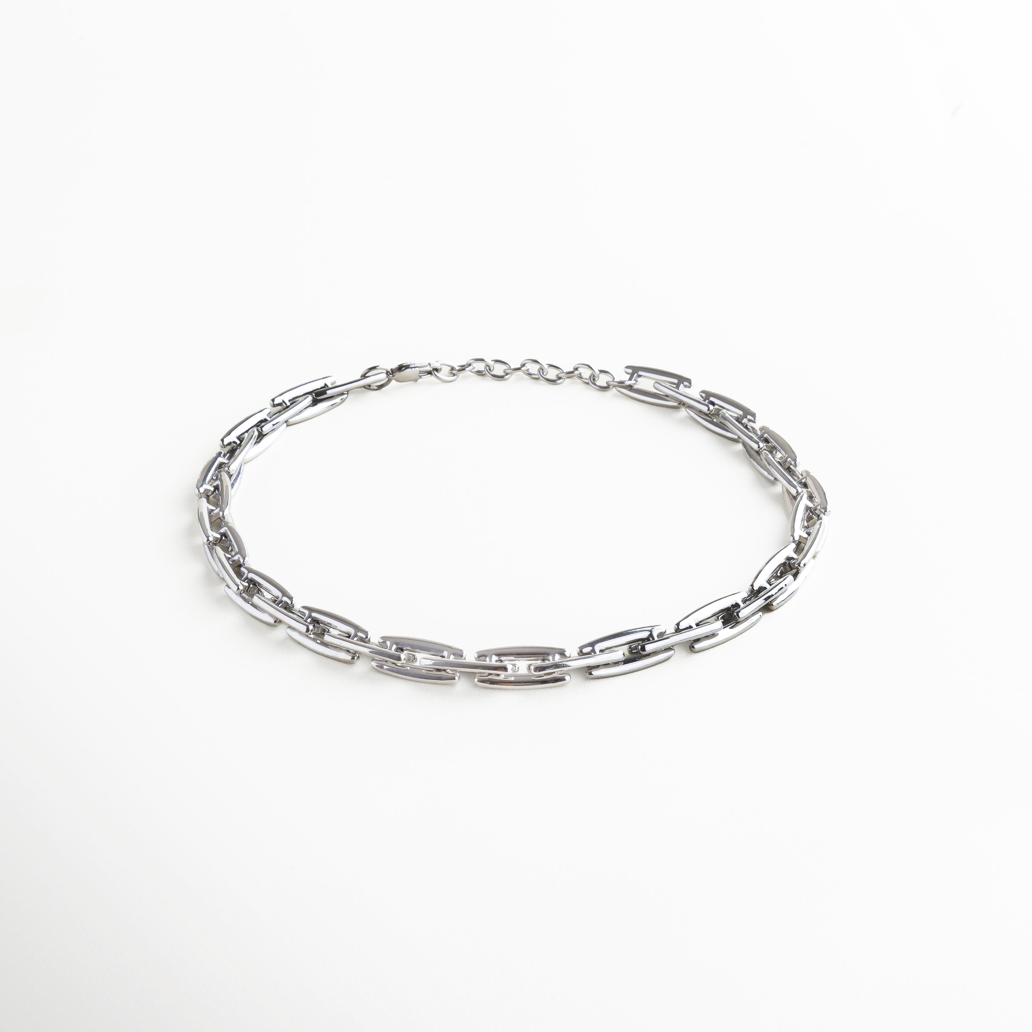 Collar plateado, cadena plateada. Collar Amelia plateado visto de perfil, con eslabones gruesos de 1 cm y caída estructurada sobre superficie neutra. Vista lateral del collar con diseño moderno, destacando su forma sólida y elegante movimiento. Perfil del Collar Amelia plateado, con eslabones planos y acabado reflectivo en acero inoxidable. Detalle lateral de los eslabones rectangulares en tono plata, con diseño contemporáneo y fuerte presencia. Collar estructurado visto desde un ángulo late