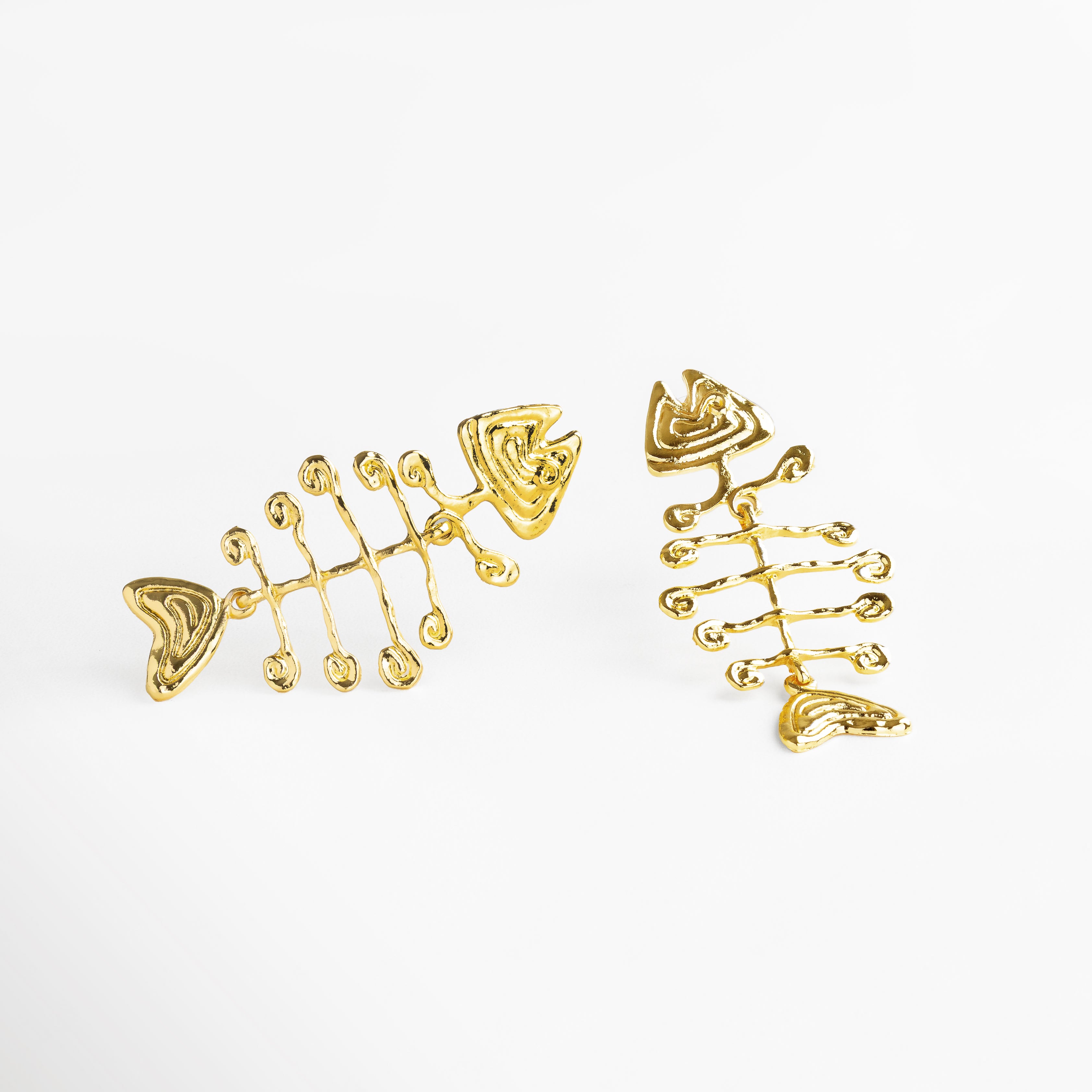 Detalle del diseño esqueletal en aretes dorados, Textura y acabado pulido en acero inoxidable dorado, Incrustaciones y líneas definidas en pendientes esqueléticos, Acabado brillante en aretes con forma orgánica