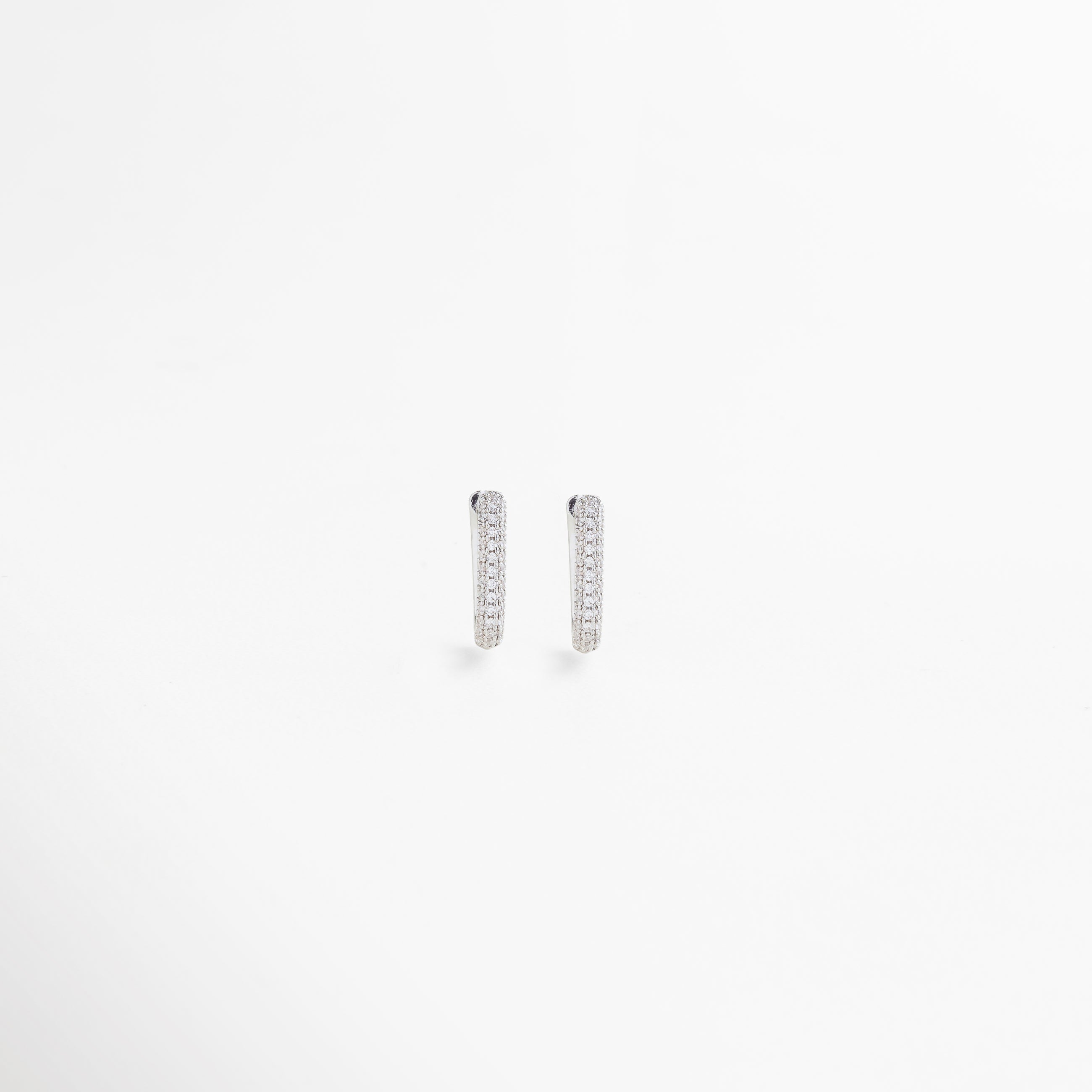 Vista frontal de aretes pequeños rectangulares en oro blanco con incrustaciones de zirconias, perfectos para un estilo sofisticado y versátil.