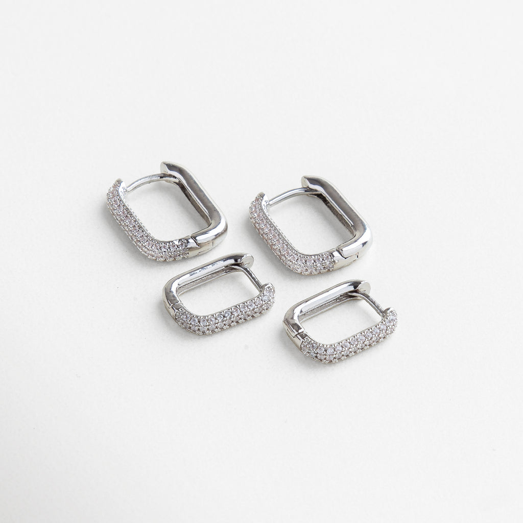 Aretes rectangulares plateados con incrustaciones brillantes, disponibles en dos tamaños, Juego de arracadas plateadas rectangulares con zirconias, diseño moderno y elegante, Aros rectangulares plateados grandes y pequeños, estilo versátil y sofisticado.