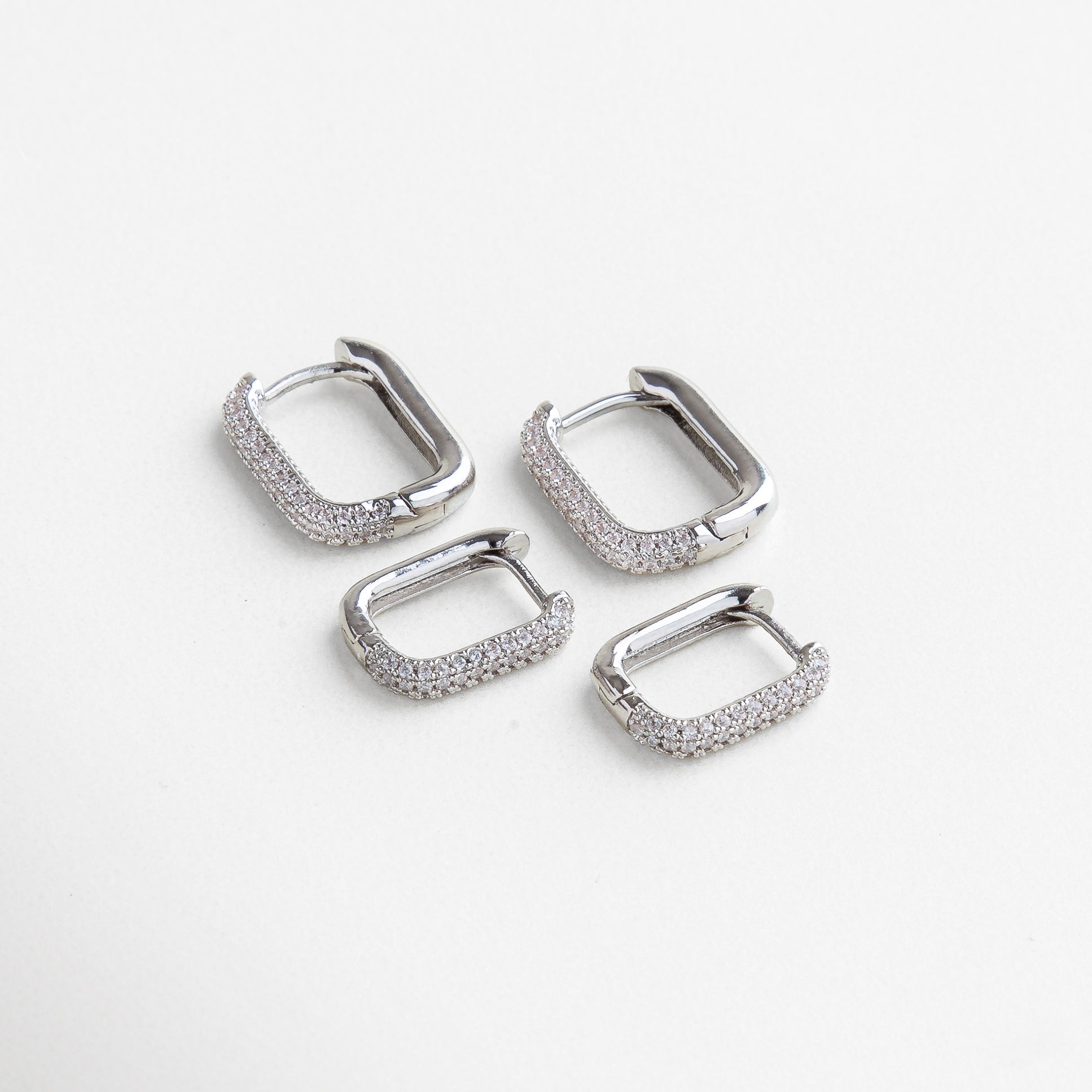 Aretes rectangulares plateados con incrustaciones brillantes, disponibles en dos tamaños, Juego de arracadas plateadas rectangulares con zirconias, diseño moderno y elegante, Aros rectangulares plateados grandes y pequeños, estilo versátil y sofisticado.
