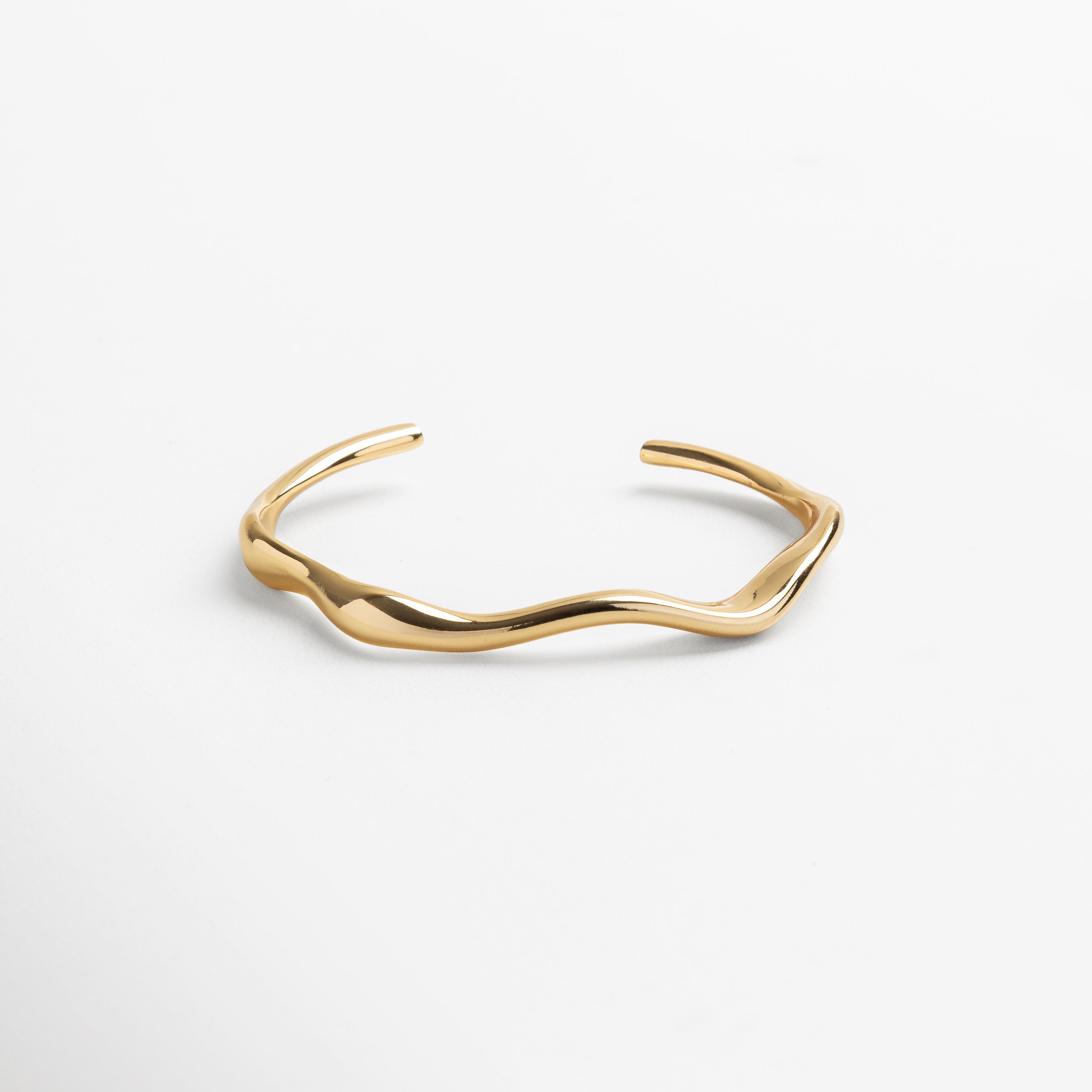 Acercamiento a la estructura rígida y forma envolvente, Diseño fluido con líneas limpias y contemporáneas, Brillo natural reflejado en la superficie del brazalete, Contraste entre interior y exterior del accesorio, Detalle del grosor y ancho del brazalete
