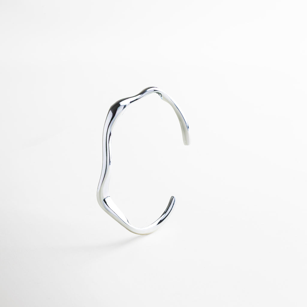 Primer plano del acabado pulido en oro blanco 18K, Detalle de la superficie lisa y diseño orgánico del brazalete, Textura metálica fina con brillo sutil, Borde del brazalete con curvatura estilizada, Acabado de alta calidad en acero inoxidable resistente
