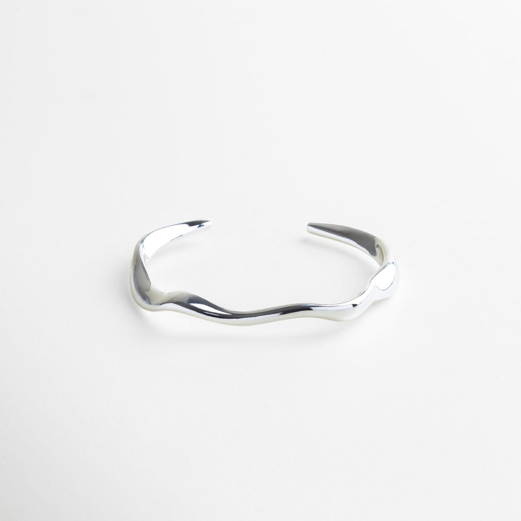 Brazalete rígido plateado con diseño orgánico contemporáneo, Pulsera minimalista en acero inoxidable con baño en oro blanco 18K, Accesorio de joyería moderno y versátil para mujer, Brazalete elegante con acabado pulido en tono plateado, Joya rígida con estilo refinado y atemporal 