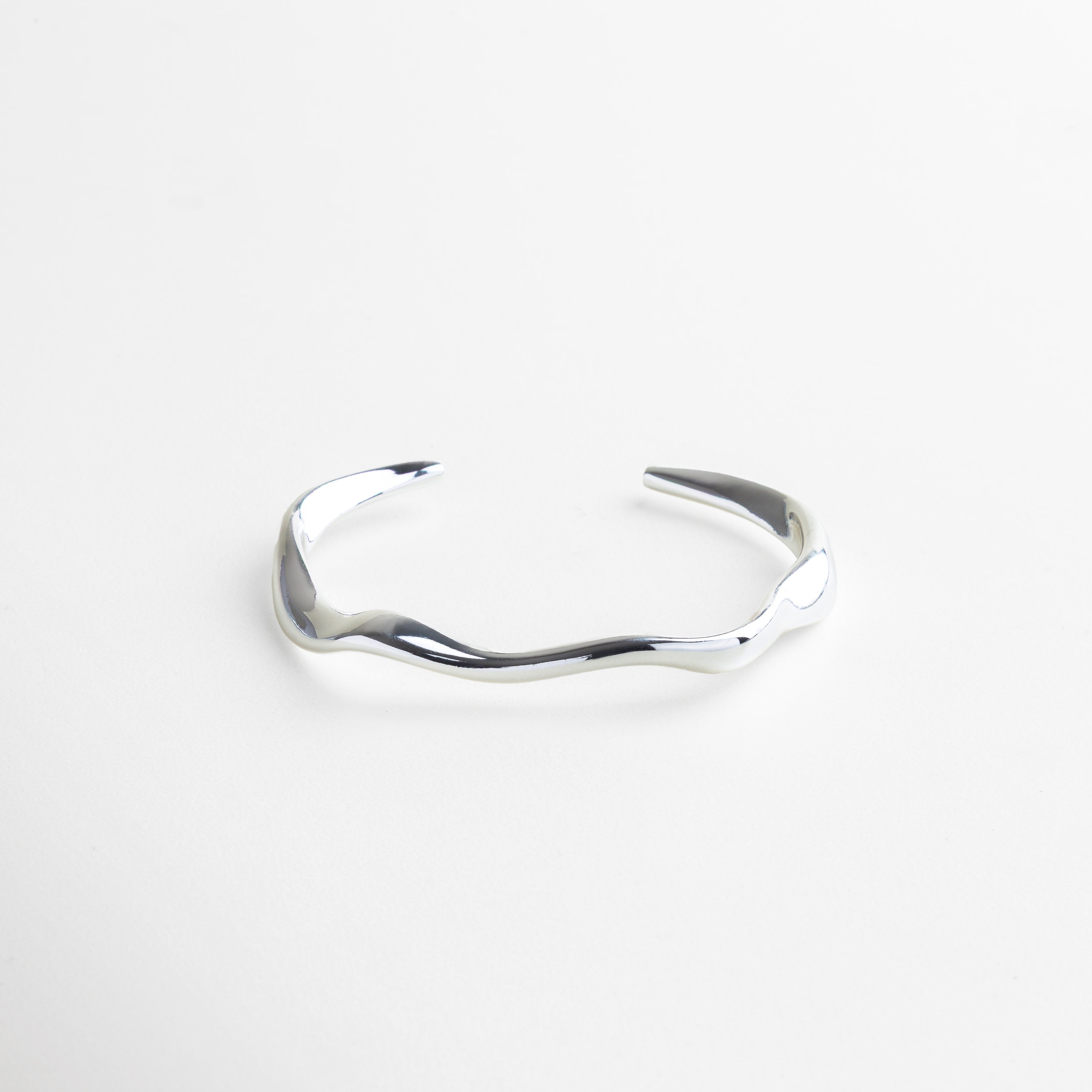 Brazalete rígido plateado con diseño orgánico contemporáneo, Pulsera minimalista en acero inoxidable con baño en oro blanco 18K, Accesorio de joyería moderno y versátil para mujer, Brazalete elegante con acabado pulido en tono plateado, Joya rígida con estilo refinado y atemporal 