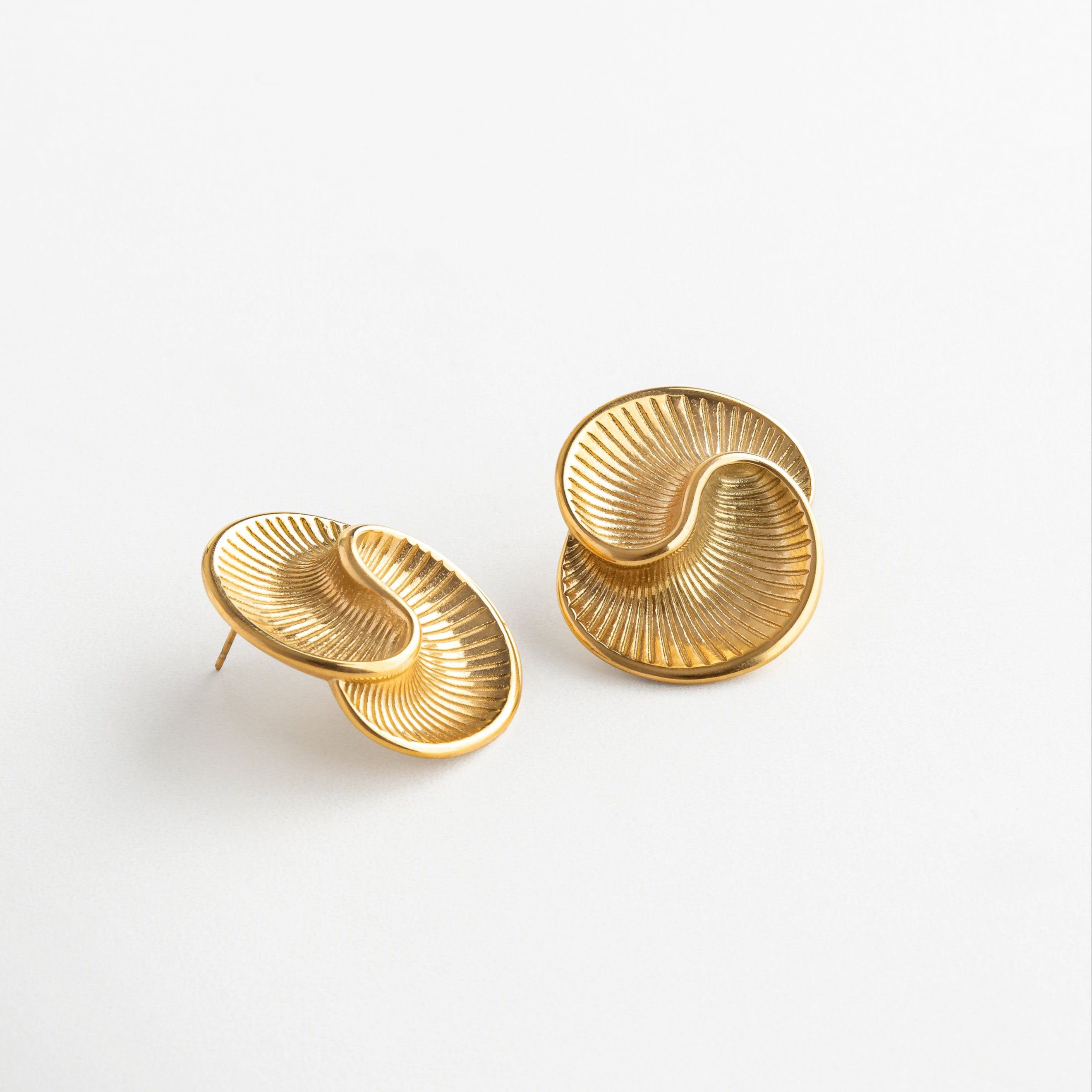 Detalle en ángulo de aretes espirales con textura facetada, Vista lateral de aretes con forma fluida y diseño escultórico, Aretes con efecto óptico en espiral y superficie facetada, Curvas elegantes con brillo sutil en ángulo