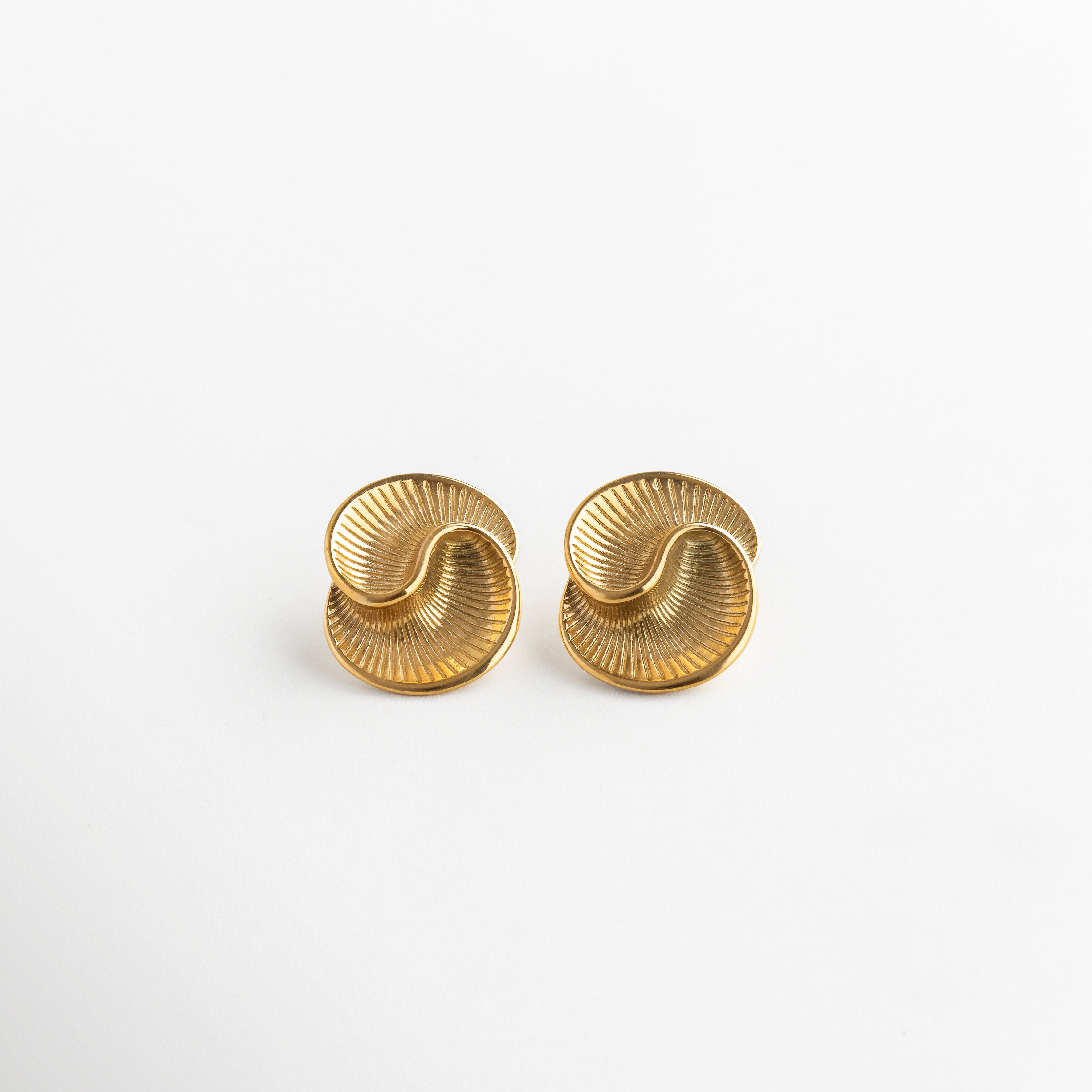 Aretes con diseño en espiral y acabado facetado, Par de aretes con forma ondulada y textura brillante, Aretes modernos en espiral que reflejan la luz, Joyería elegante con líneas curvas y estilo contemporáneo