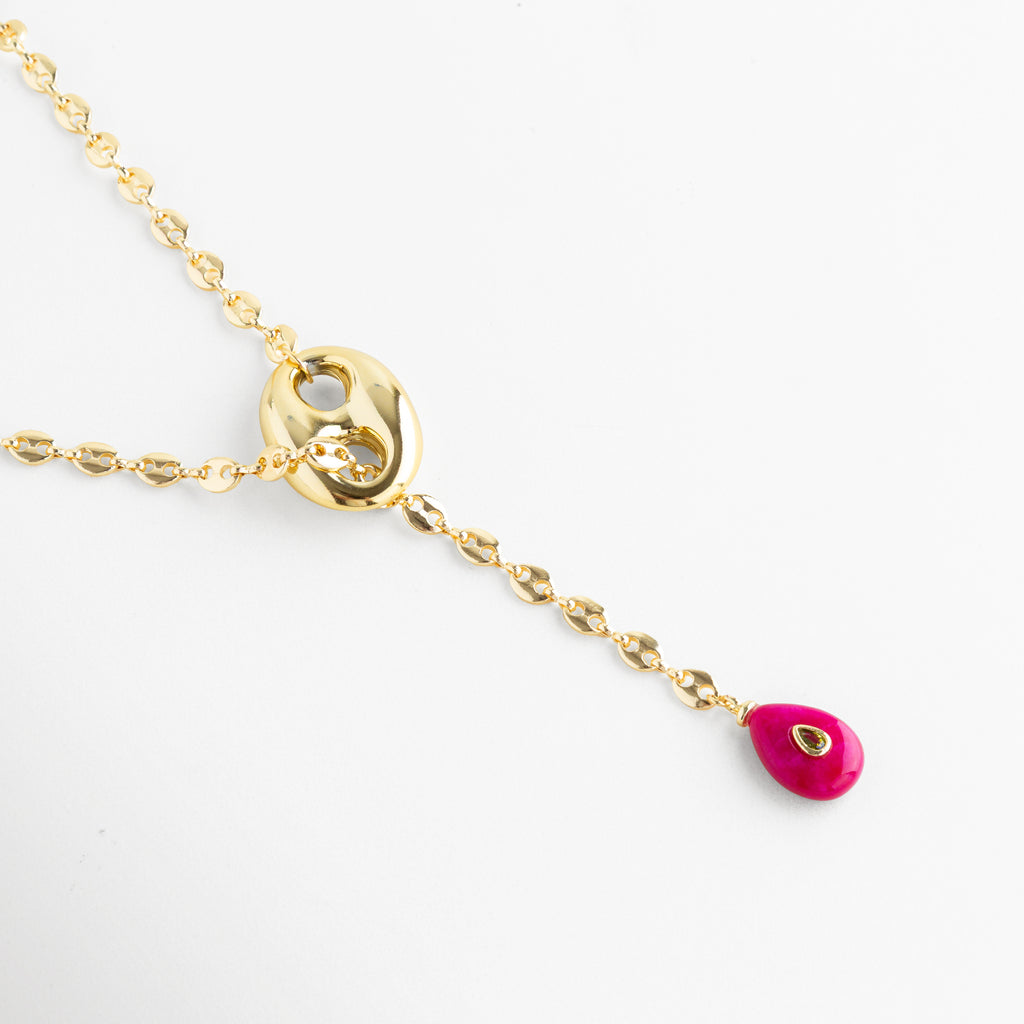 Collar Liriana de cobre con baño de oro 18K y dije de gota fucsia con zirconia, Detalle de cadena estilo grano de café dorada con incrustación de zirconia brillante, Joyería elegante: collar dorado con piedra fucsia vibrante y detalle central ovalado, Vista de cerca de collar enchapado en oro 18K con terminal en forma de gota rosa.
