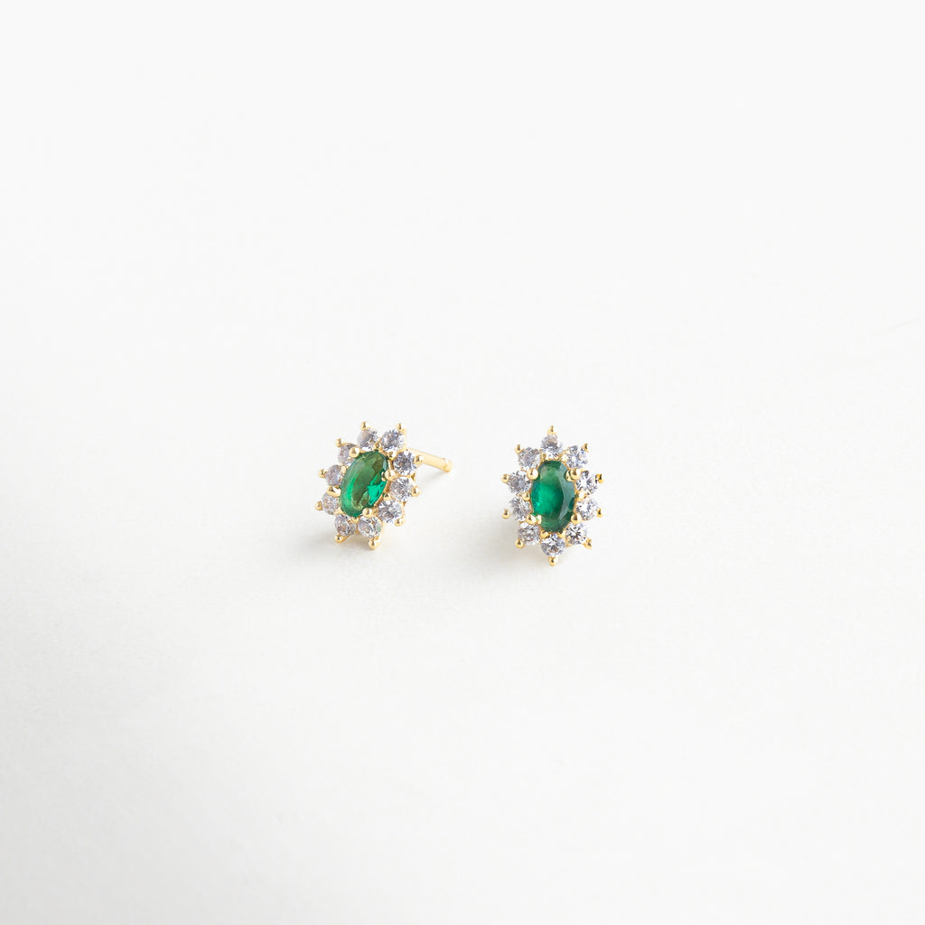 Vista en ángulo de broqueles florales con brillo sutil, Detalle lateral de pendientes con piedra verde y pétalos, Aretes con forma orgánica y toque esmeralda vistos en perfil, Diseño tridimensional de flor con centro en tono esmeralda