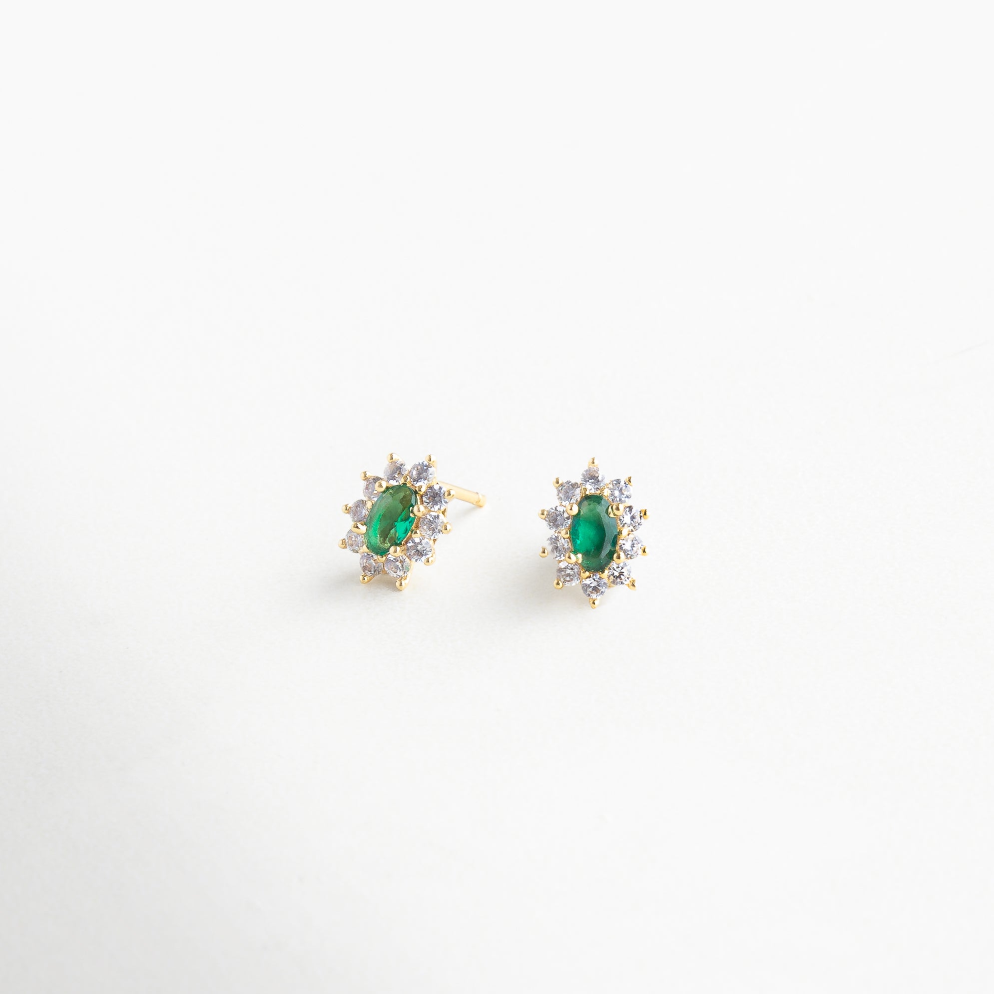 Vista en ángulo de broqueles florales con brillo sutil, Detalle lateral de pendientes con piedra verde y pétalos, Aretes con forma orgánica y toque esmeralda vistos en perfil, Diseño tridimensional de flor con centro en tono esmeralda