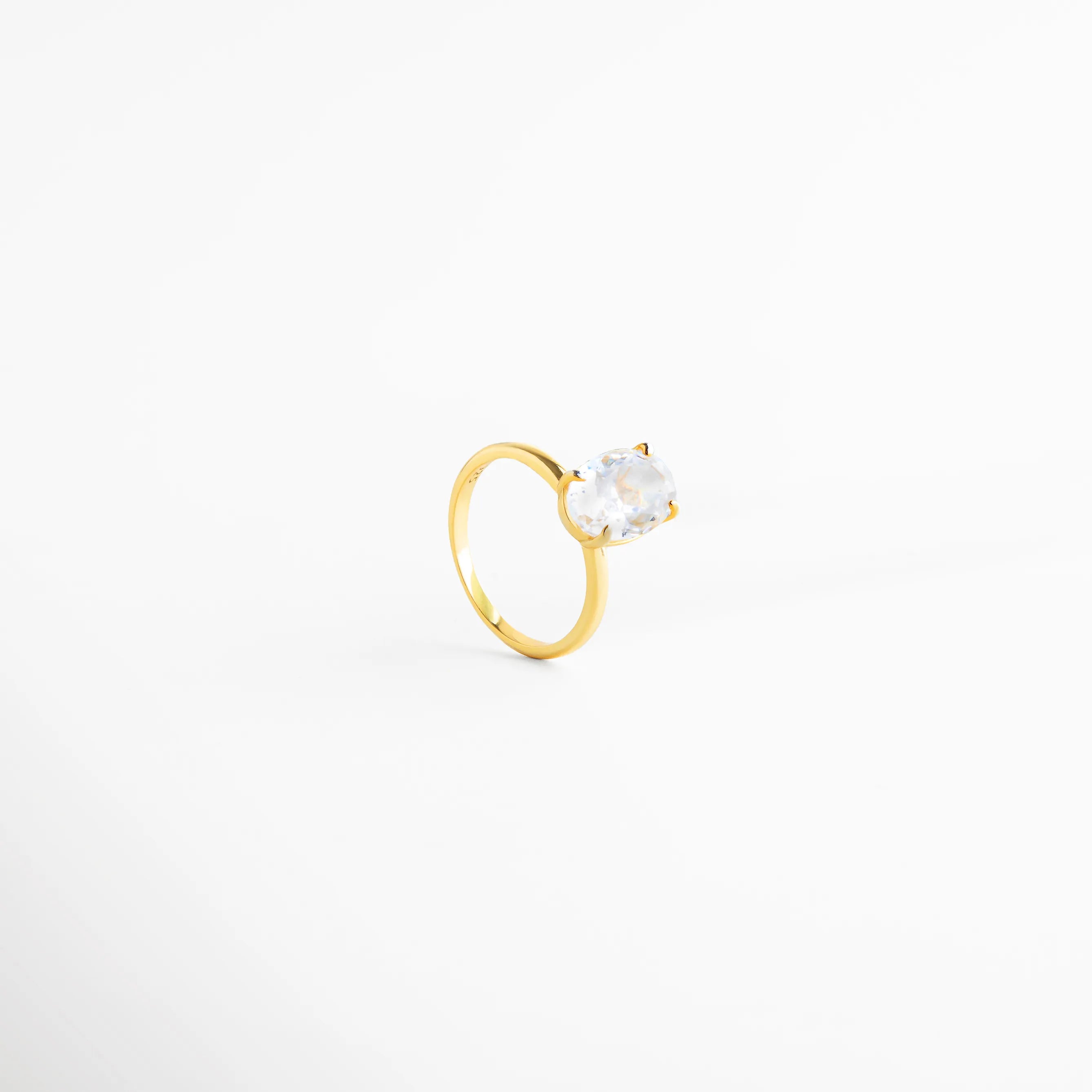 anillo dorado con zirconia oval centrada, anillo elegante vista superior brillante, anillo clásico dorado joyería fina, anillo minimalista con piedra clara, anillo dorado refinado, anillo femenino de diseño atemporal