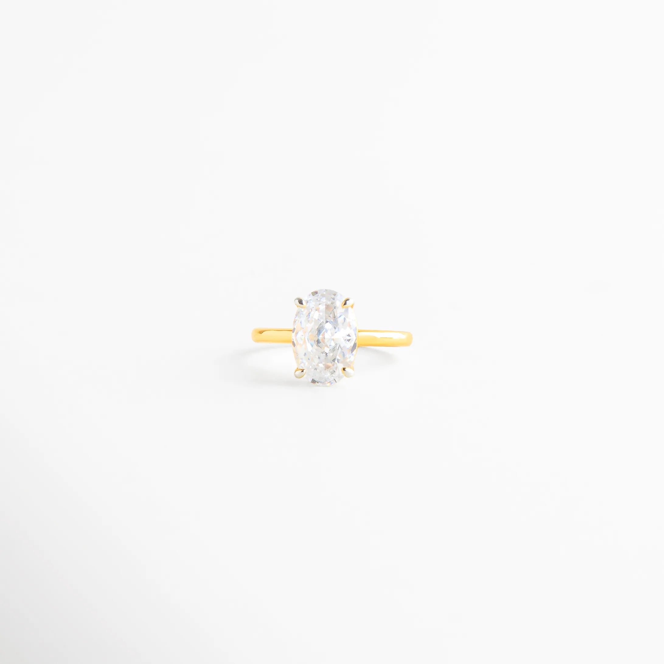 anillo dorado delicado con piedra ovalada transparente, anillo minimalista con zirconia central elegante, anillo fino dorado estilo clásico moderno, joyería femenina anillo oval sofisticado, anillo dorado brillante fondo blanco, anillo elegante de uso diario dorado
