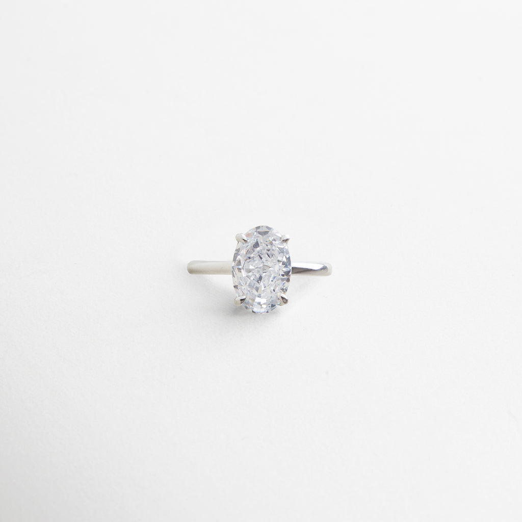anillo plateado con piedra central ovalada de zirconia cúbica, acabado impecable en oro blanco 18K, diseño elegante y atemporal, pieza que simboliza momentos duraderos, joya versátil para cualquier ocasión