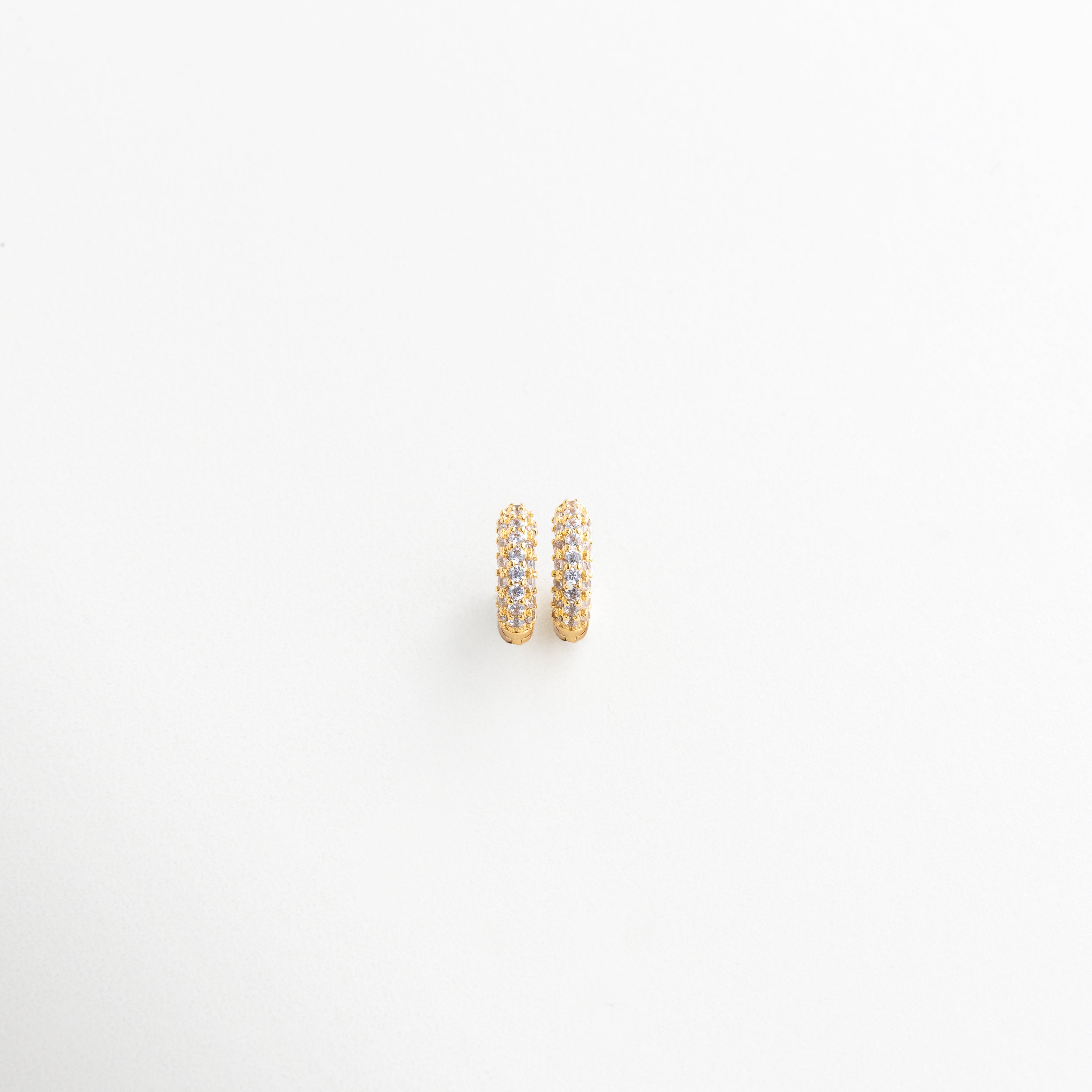 Aros mini vistos en ángulo con detalle de zirconias, Vista lateral de pendientes dorados tipo círculo, Diseño curvo de arracadas pequeñas con brillo sutil, Mini hoops elegantes con textura brillante