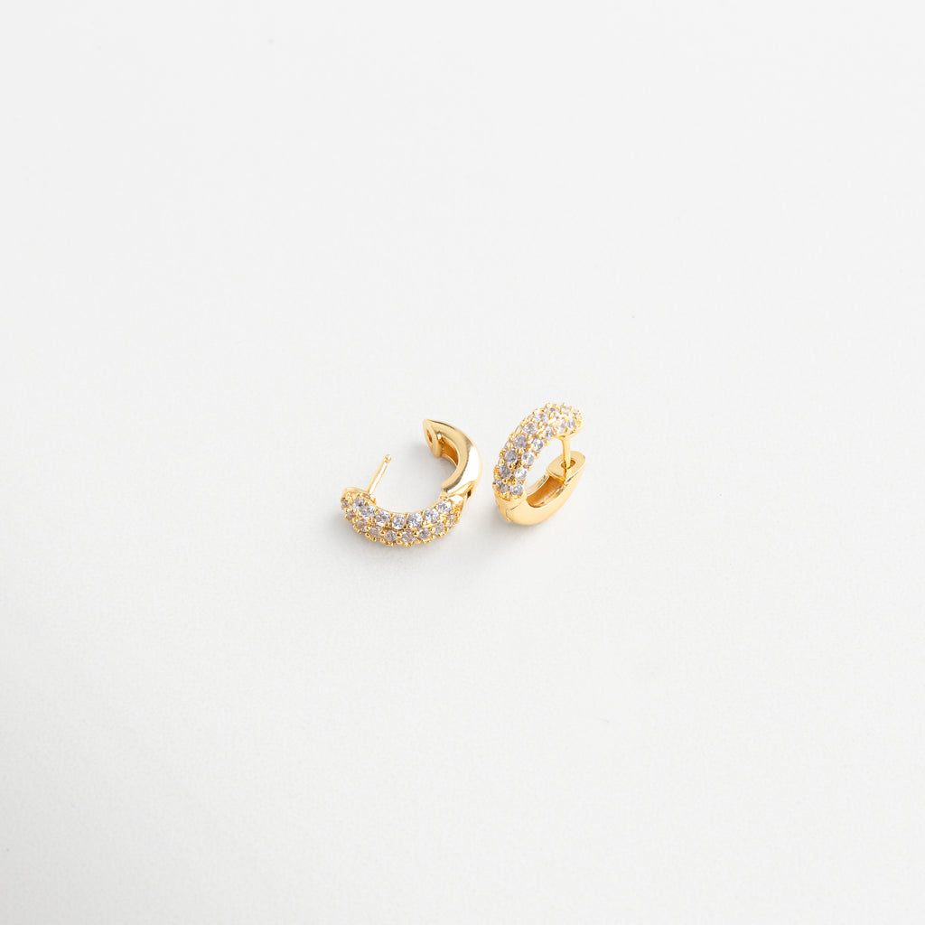 Close-up de zirconias en mini hoops dorados, Detalle de incrustaciones en aros pequeños, Textura brillante de pendientes mini circulares, Diseño depurado con brillo en primer plano