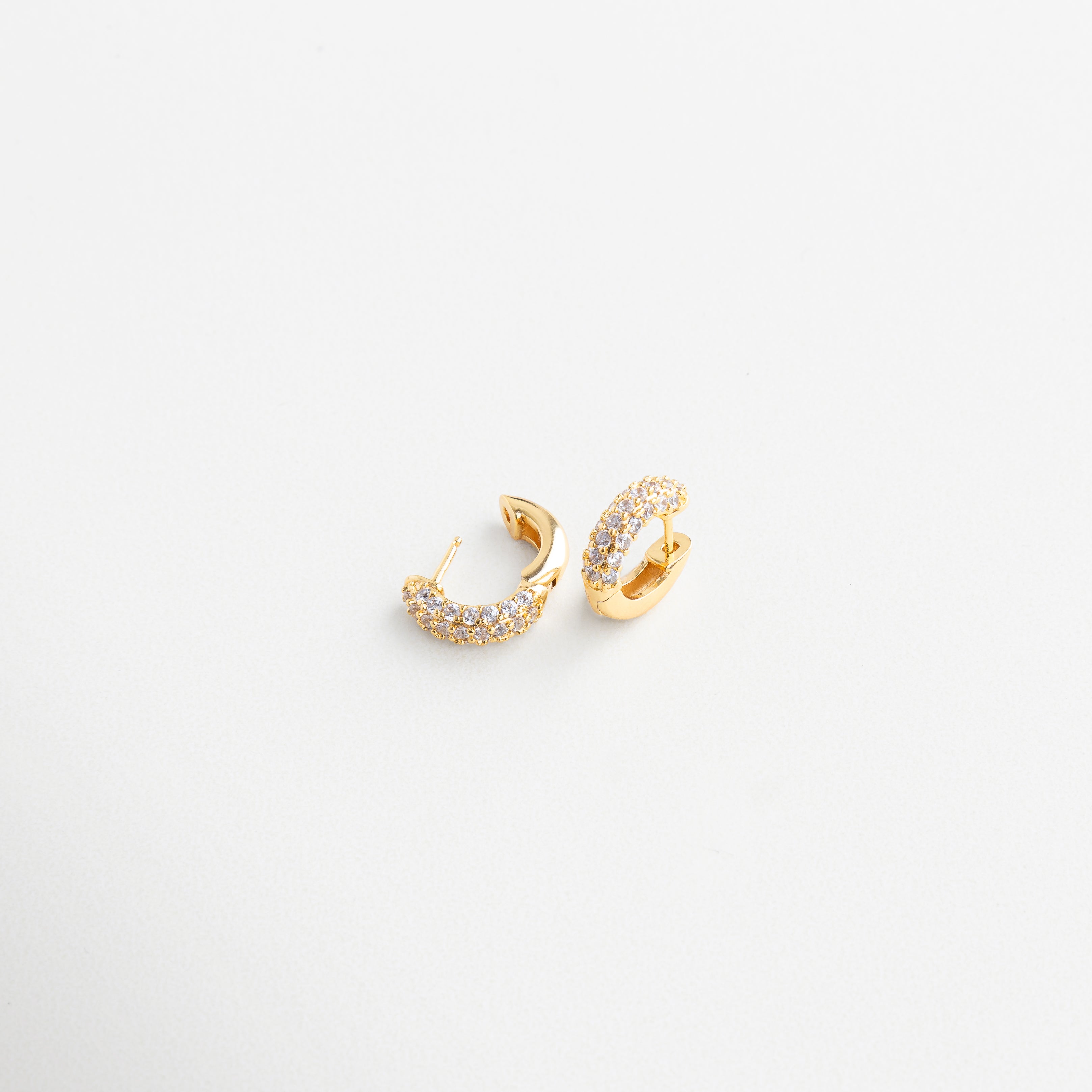 Close-up de zirconias en mini hoops dorados, Detalle de incrustaciones en aros pequeños, Textura brillante de pendientes mini circulares, Diseño depurado con brillo en primer plano