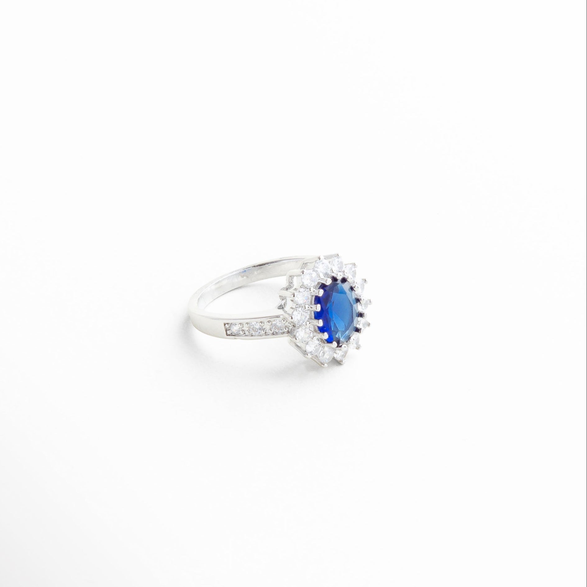 centro ovalado azul con marco de zirconias, engarzado fino con diamantes y piedra central azul, detalles brillantes que rodean la zirconia azul, textura pulida del aro con incrustaciones delicadas, brillo facetado del centro azul profundo