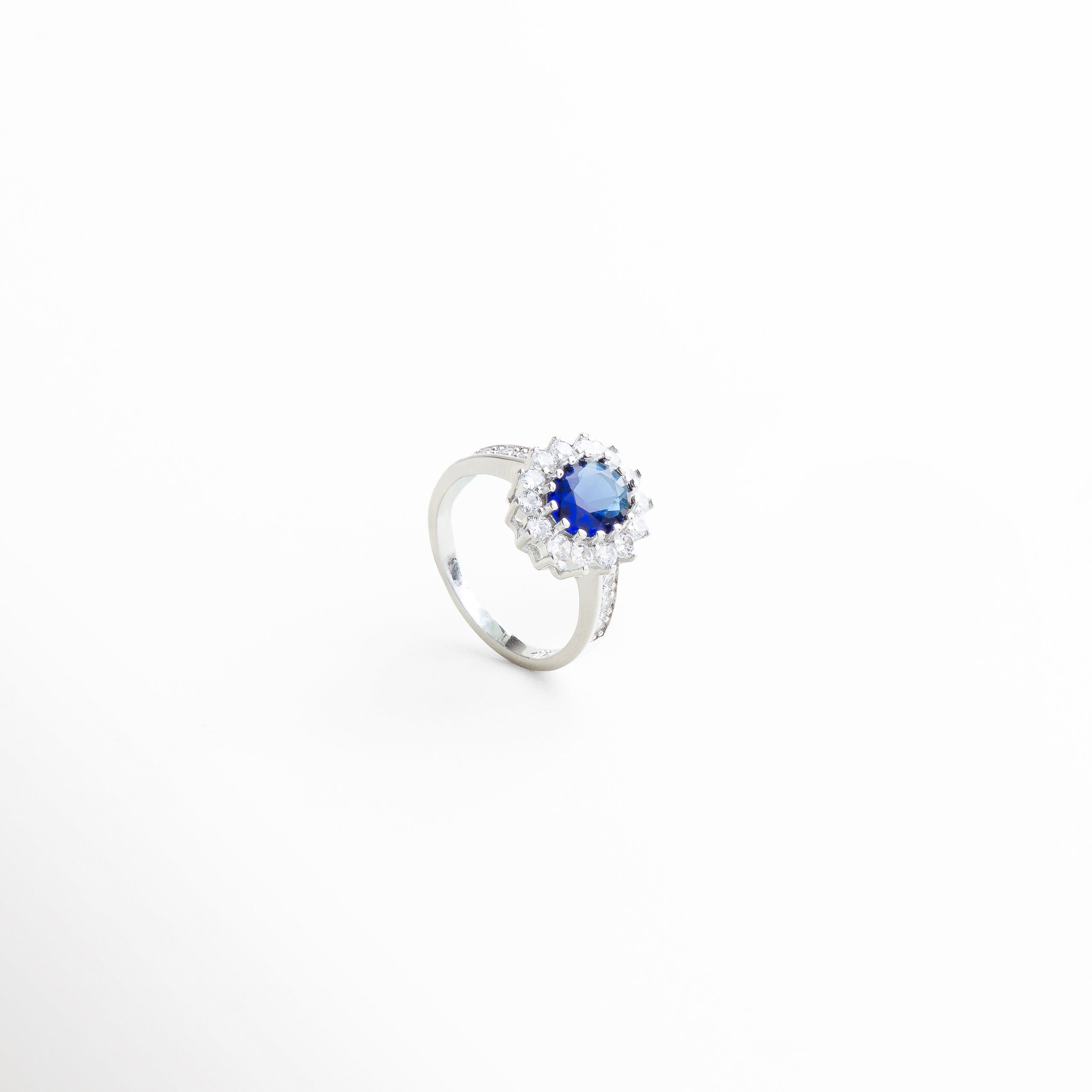 escala del anillo con centro azul en la mano, proporción del aro y la piedra principal en contexto, tamaño real del anillo brillante con centro ovalado, vista comparativa del anillo con joyería complementaria, dimensión visual del diseño con halo y piedra azul