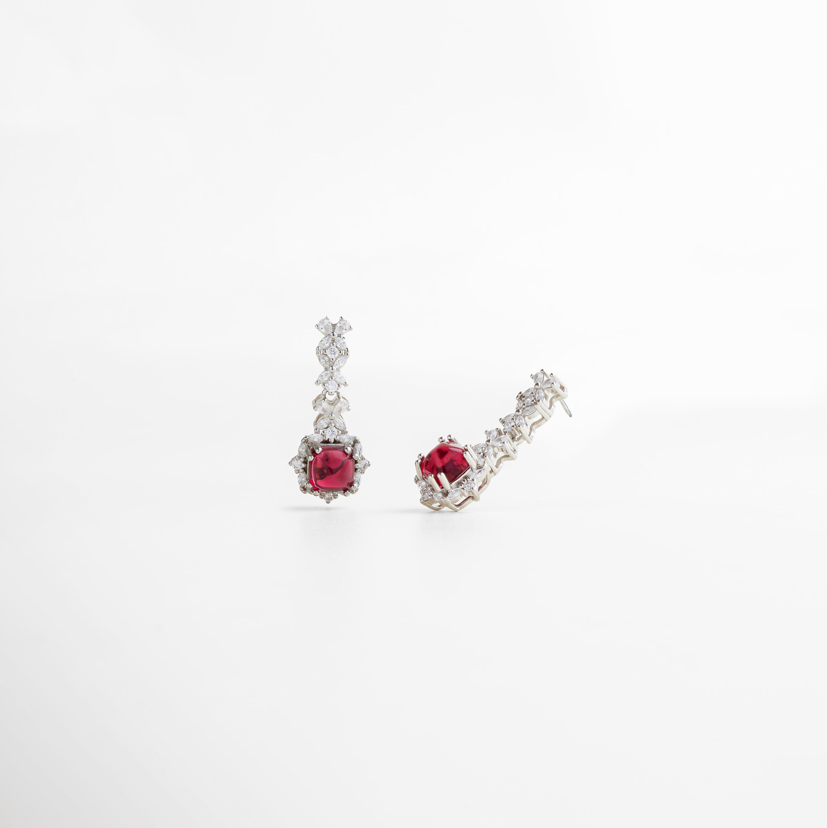 enfoque en el brillo de la piedra, tonalidad rubí intensa y pulida, recubrimiento enchapado en plata de alta calidad, aretes de diseño llamativo y elegante, pieza diseñada para destacar con sutileza