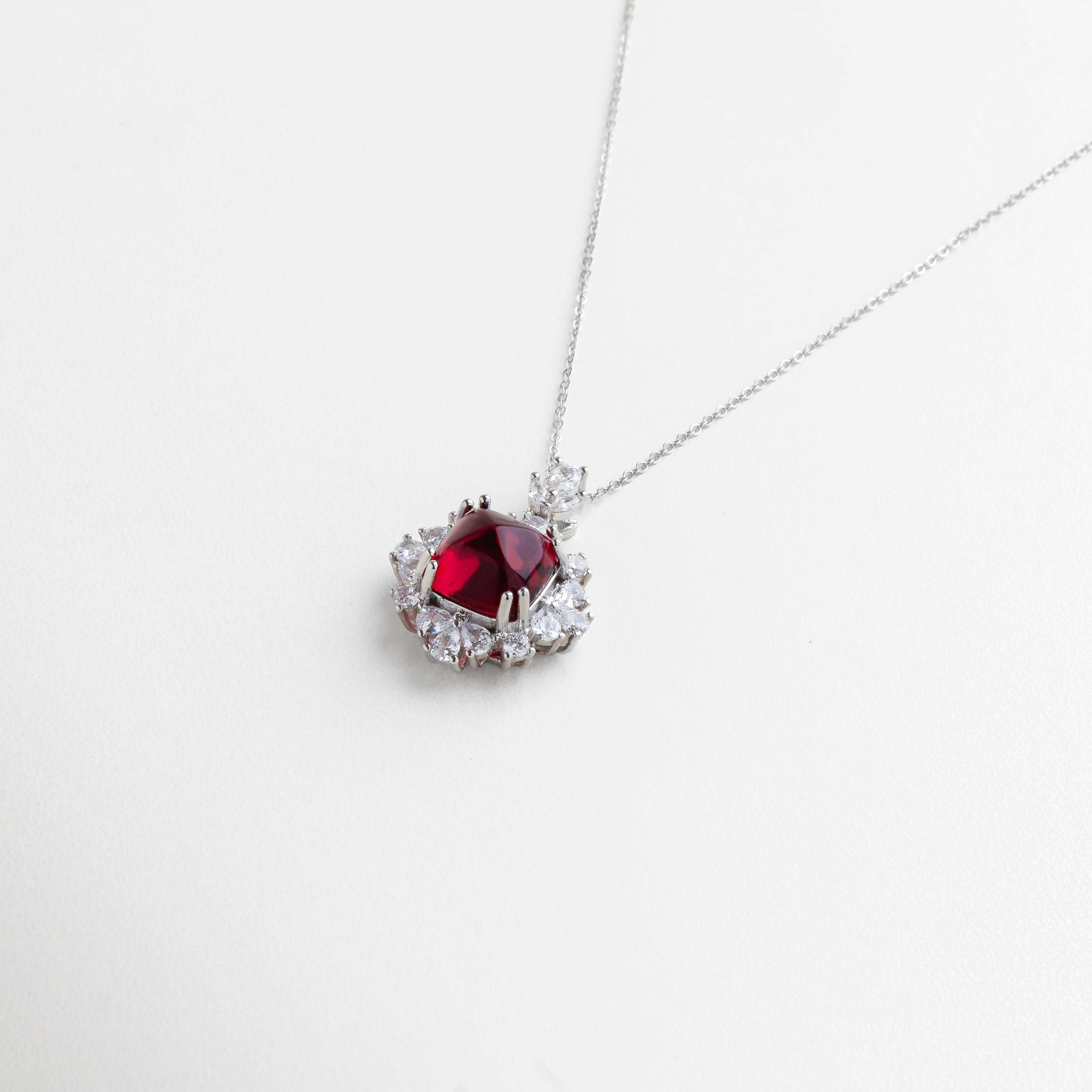 enfoque en la zirconia rubí central, corte preciso que maximiza el brillo, engaste detallado y pulido, contraste entre piedra roja y halo cristalino, diseño que equilibra sutileza y glamour