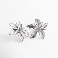 Aretes plateados con forma de flor tridimensional, Pendientes grandes con diseño artístico y textura marcada, Aretes florales en acabado plateado brillante, Joyería escultórica en forma de flor en movimiento
