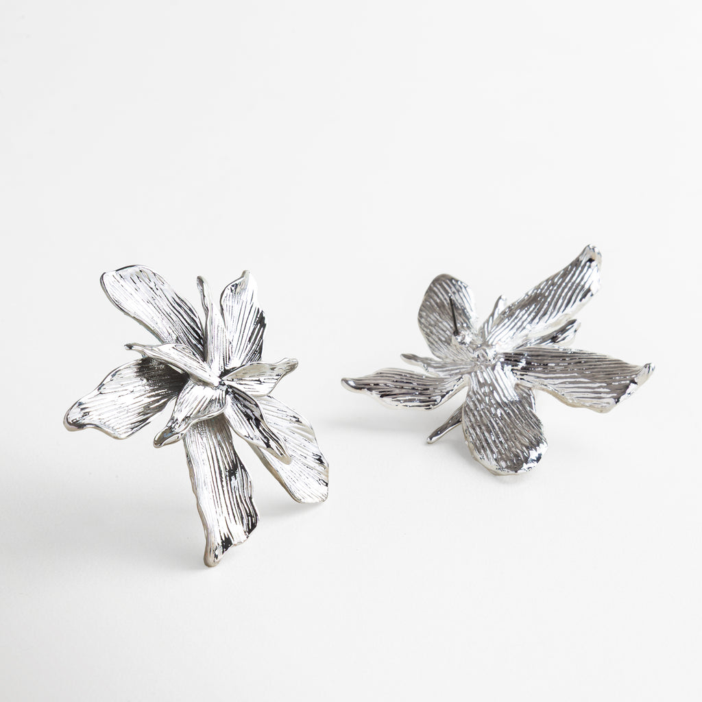 Perfil de aretes florales en baño de plataRelieve y volumen de aretes plateados desde ángulo lateral, Movimiento y forma escultórica de los pendientes, Vista en ángulo que resalta la forma orgánica 