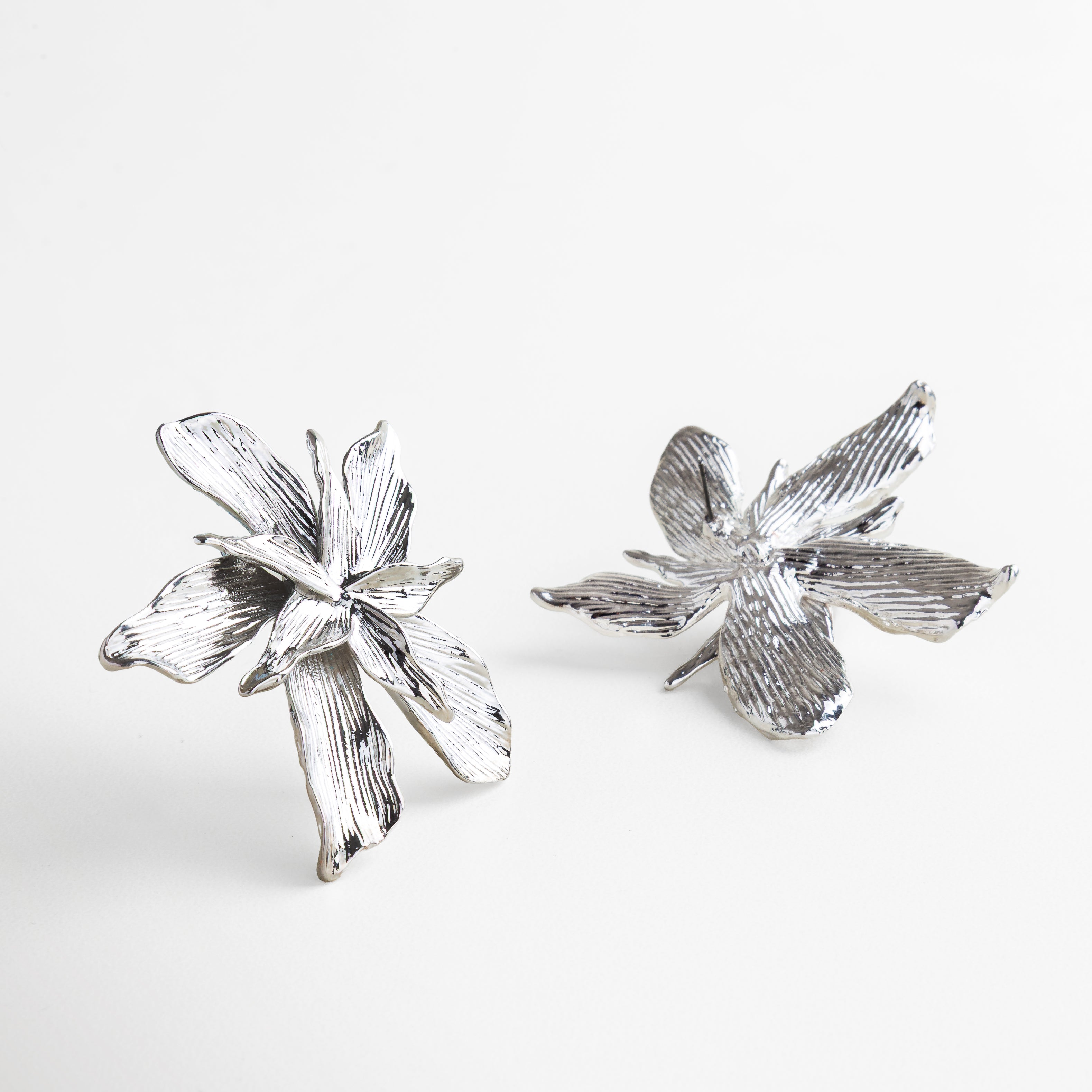 Perfil de aretes florales en baño de plataRelieve y volumen de aretes plateados desde ángulo lateral, Movimiento y forma escultórica de los pendientes, Vista en ángulo que resalta la forma orgánica 