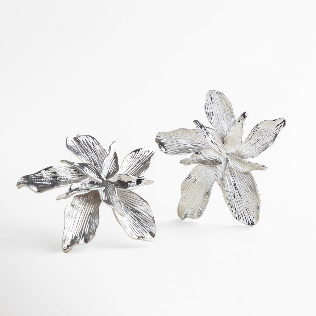 Detalle de textura orgánica en aretes plateados, Superficie brillante y marcada en pendientes de flor, Acabado pulido con efecto tridimensional, Diseño floral plateado con textura artística
