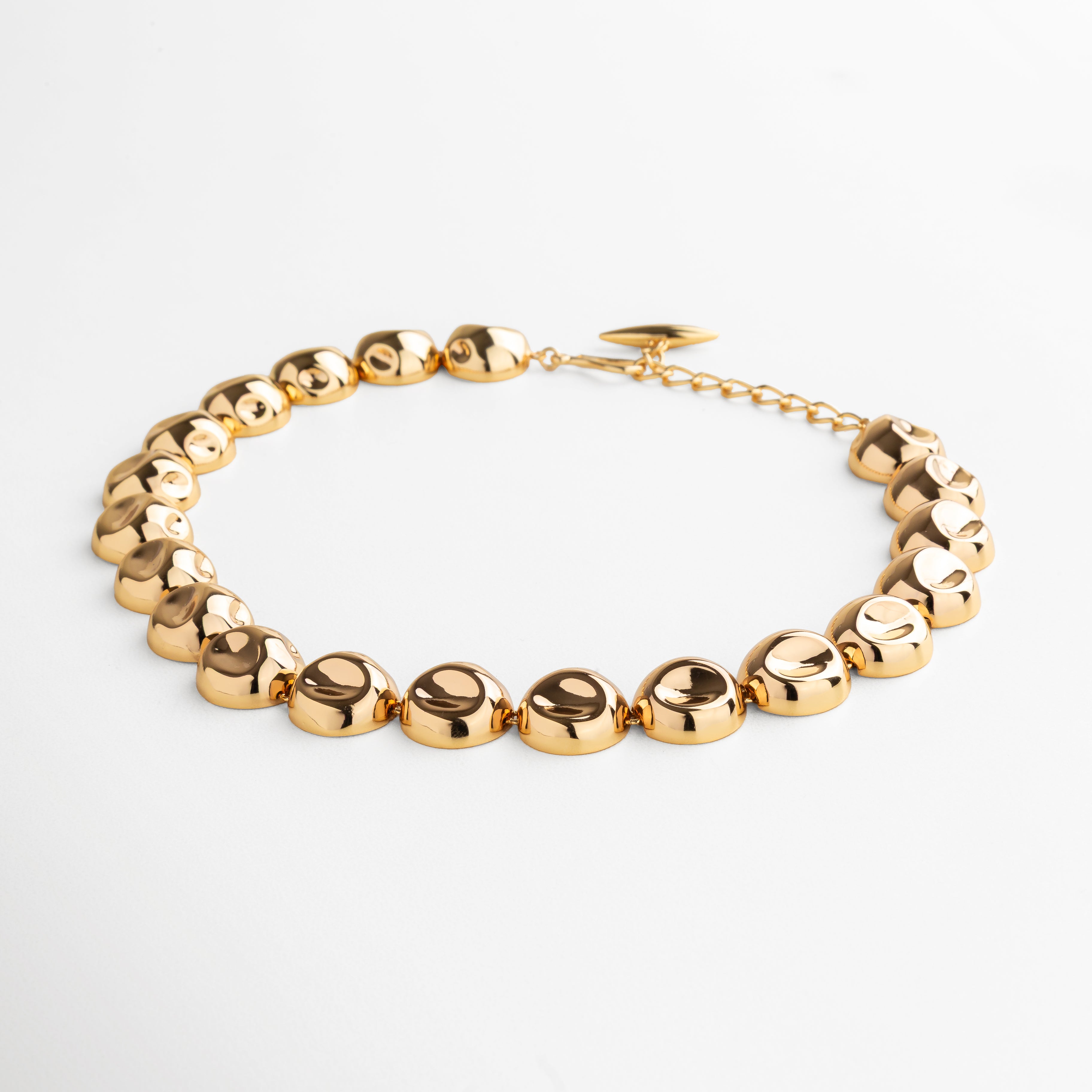 Collar Golden Bell dorado visto de perfil, mostrando la forma y grosor de los dijes unidos. Vista lateral del collar con dijes circulares, resaltando la continuidad y acabado pulido en oro 24K. Perfil del collar con diseño de dijes unidos, ideal para un look moderno y sofisticado. Detalle lateral del Collar Golden Bell, captando la textura y el brillo uniforme de los dijes. Collar con dijes circulares en acabado dorado visto desde un ángulo lateral, mostrando su estructura y estilo.